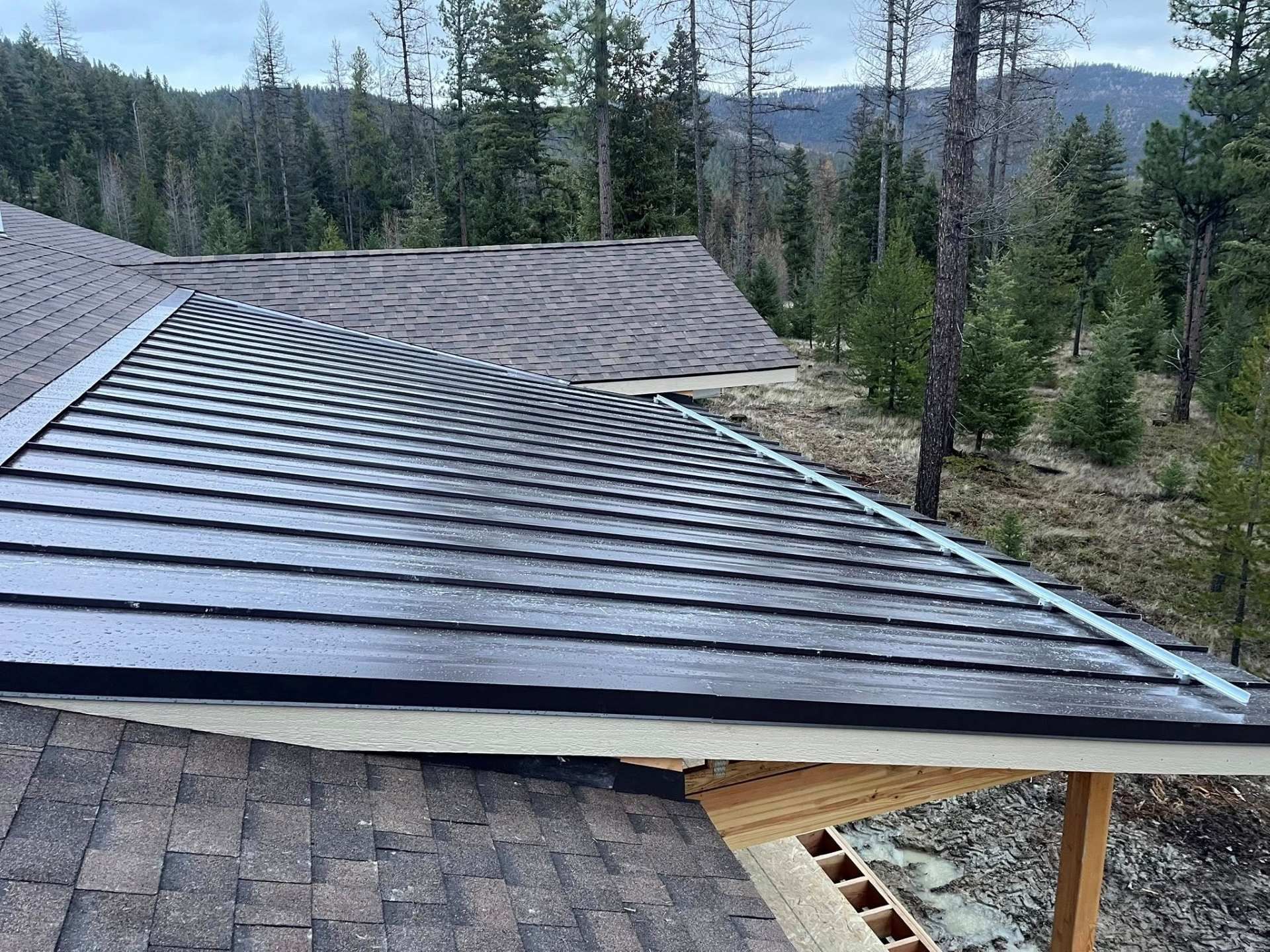 Roof under construction with metal shingles on a cabin, overlooking a forested mountain landscape