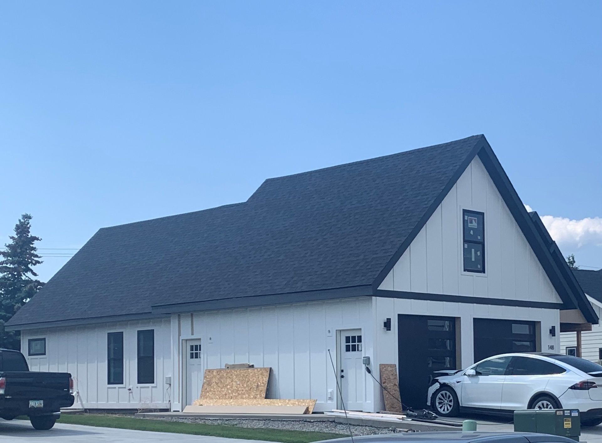 Modern white house with black roof, garage, and parked cars under a clear blue sky