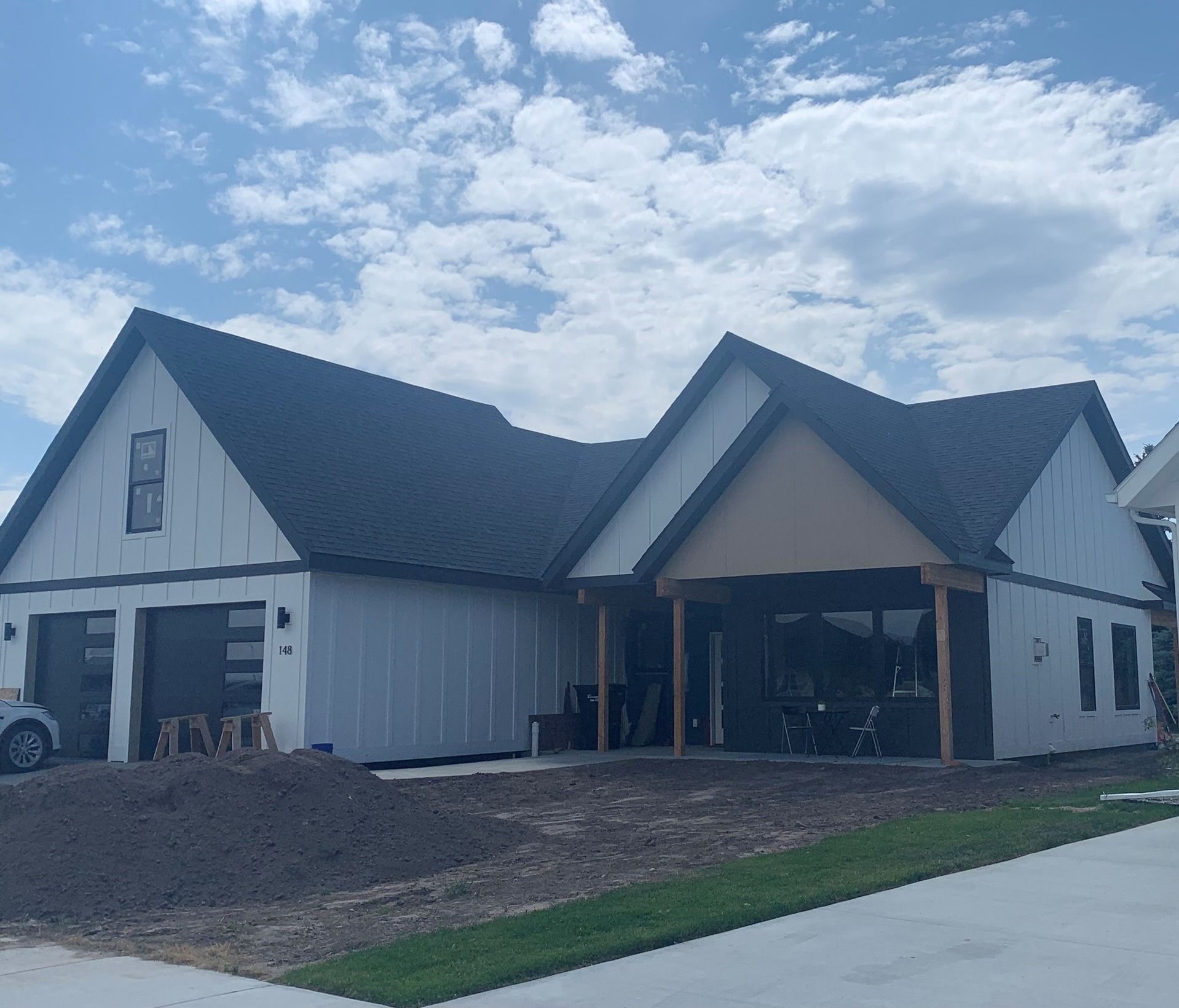 Modern farmhouse-style home under construction with gray siding, black roof, and a covered front porch.