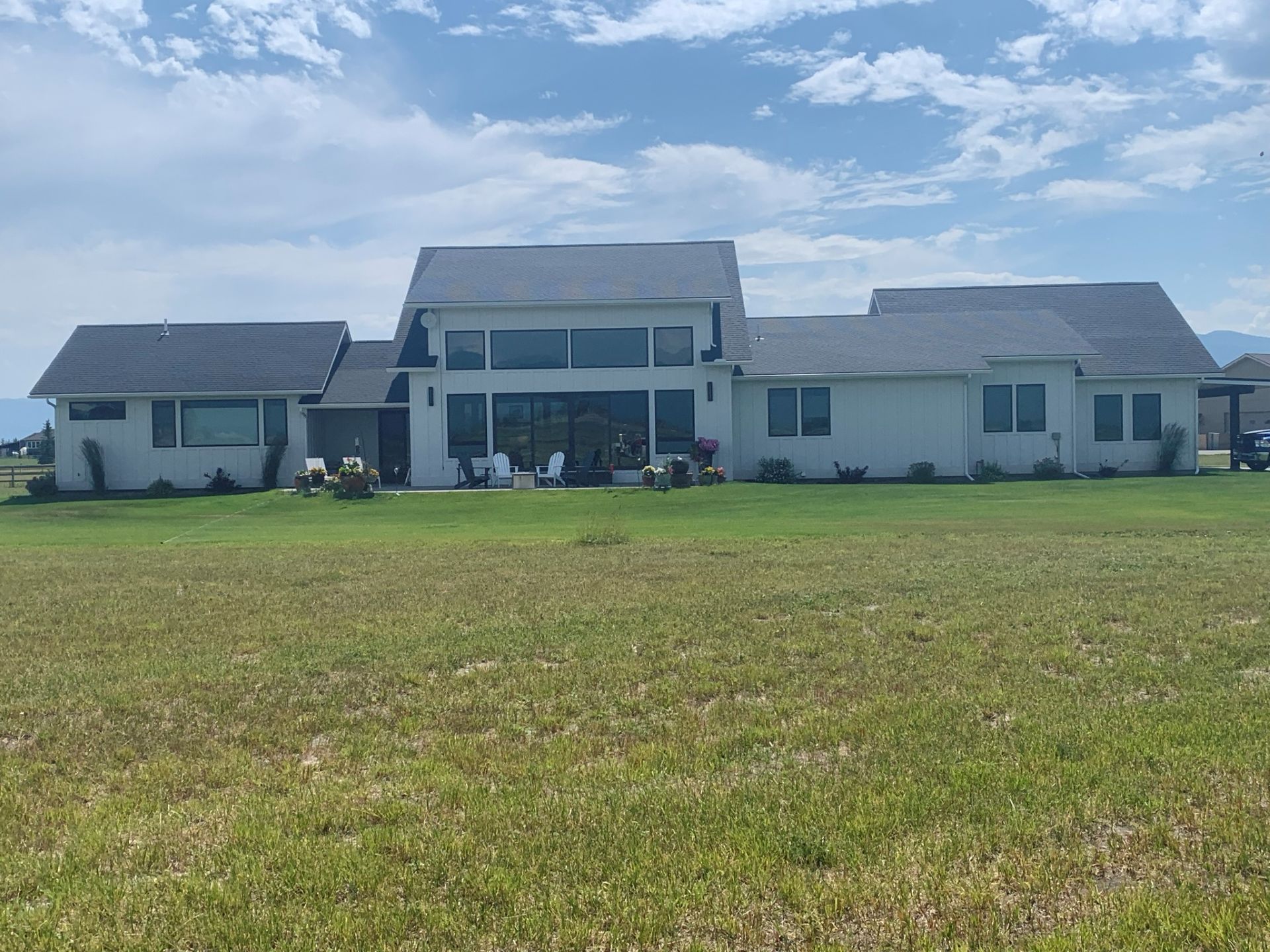 Large white house with a gray roof on a wide green lawn under a cloudy sky