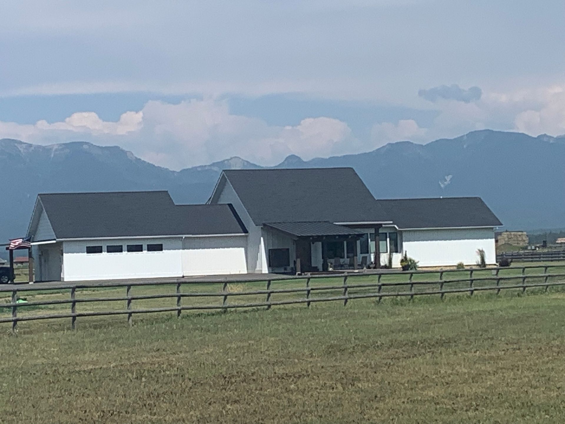 Modern farmhouse in a grassy field with mountains and cloudy sky in the background