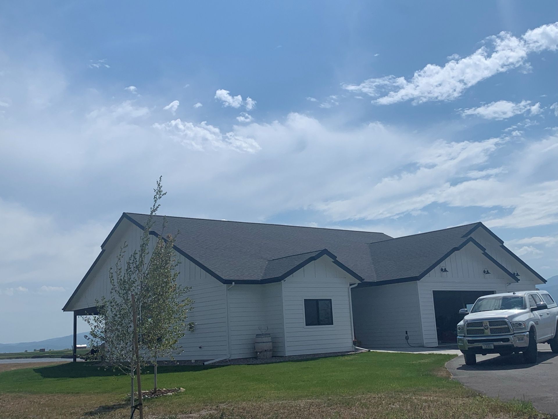 White house with gray roof on a grassy lot under a cloudy blue sky, with a truck parked at the driveway