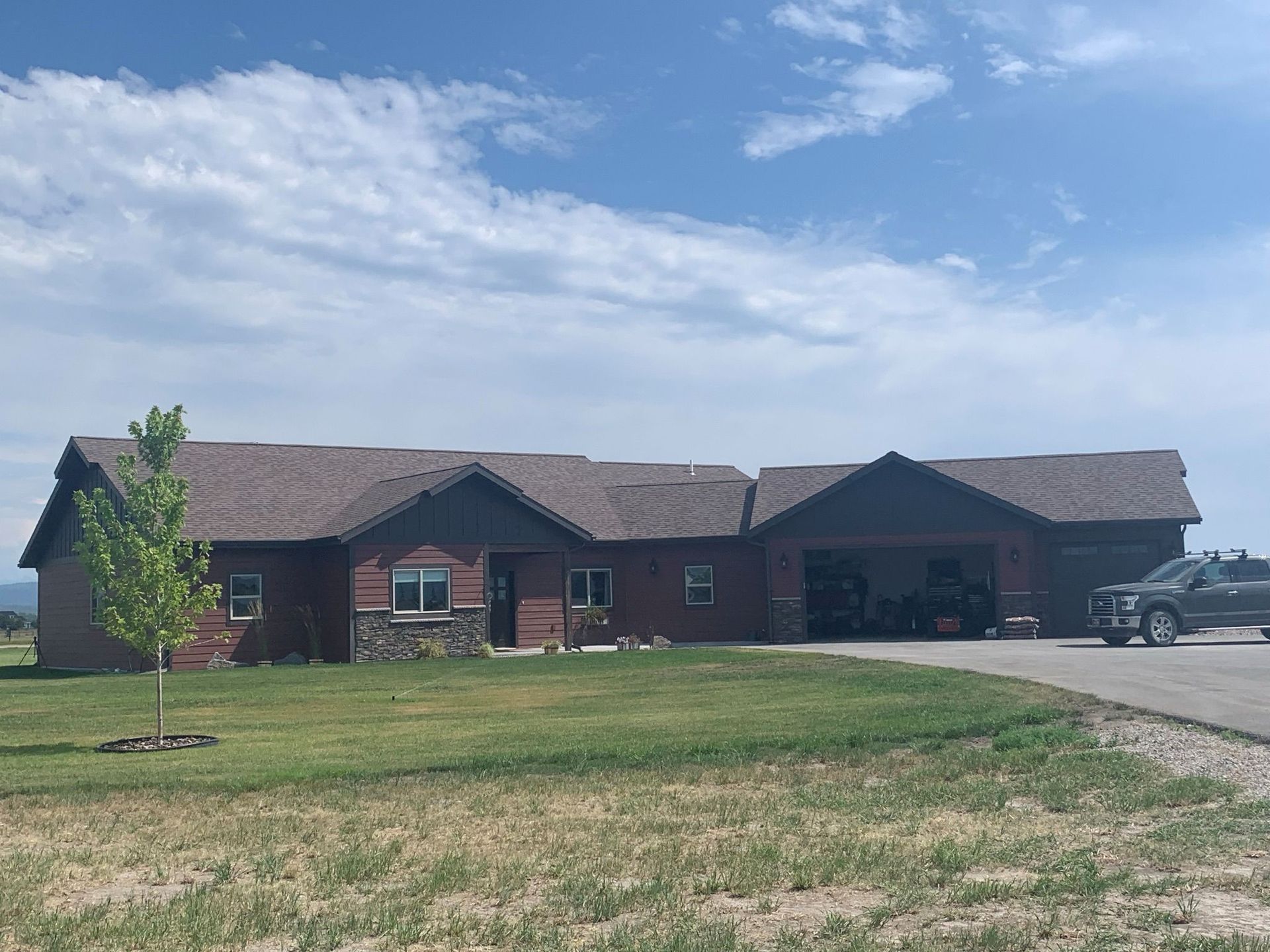 Single-story brick house with a large driveway, lawn, and partly cloudy sky