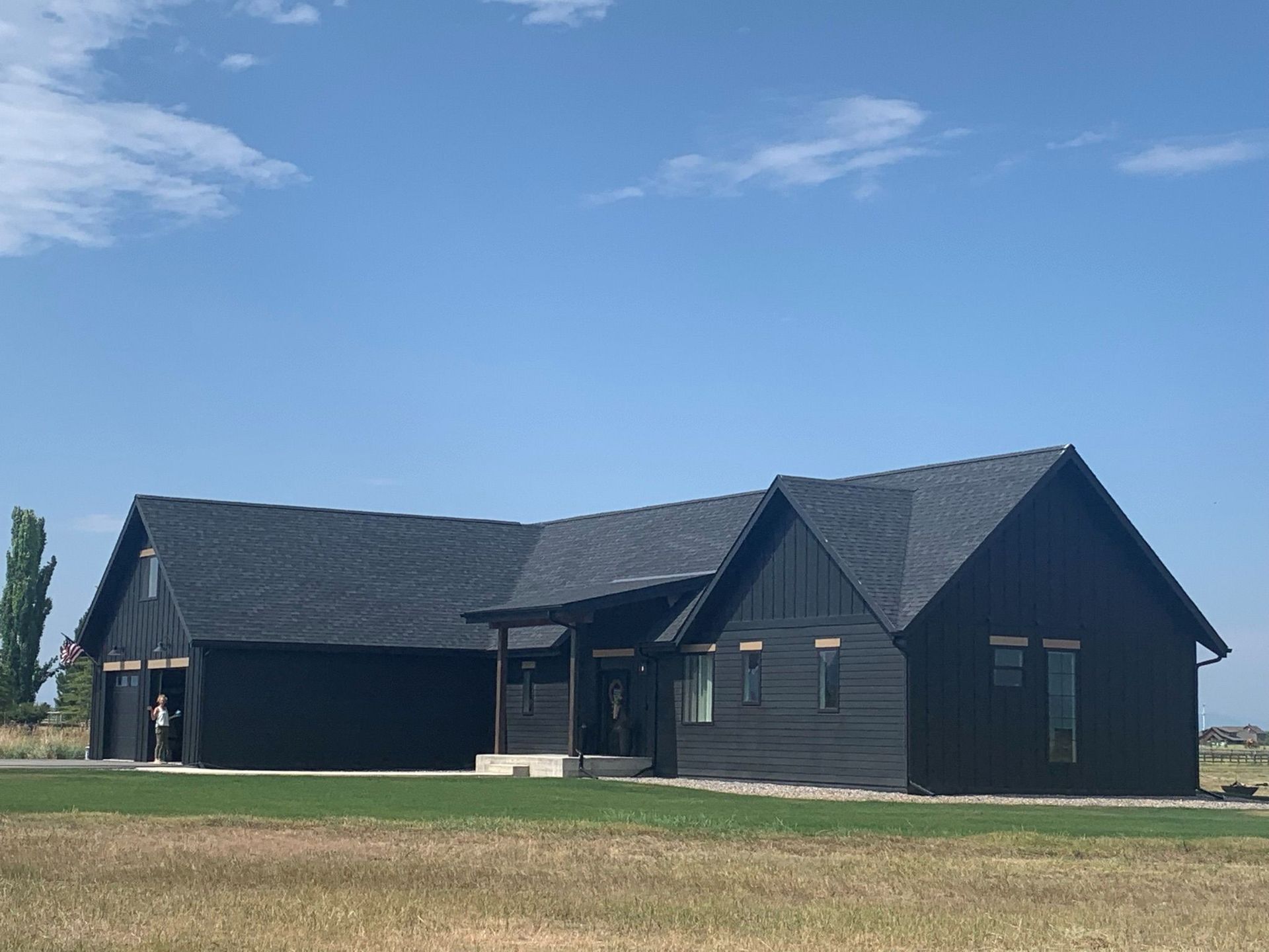 Black house with dark roof on a grassy field under a blue sky