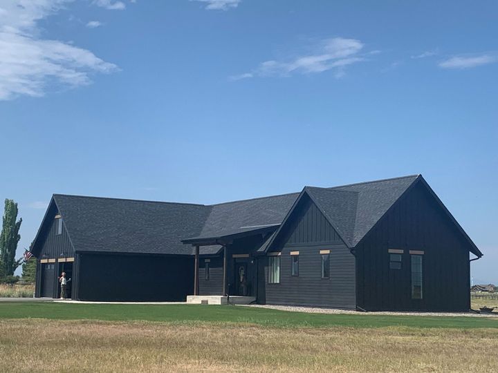 Dark gray modern house with a sloped roof on a grassy lot under a blue sky