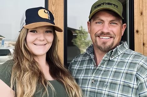 Two people smiling outdoors, wearing baseball caps and casual plaid shirts