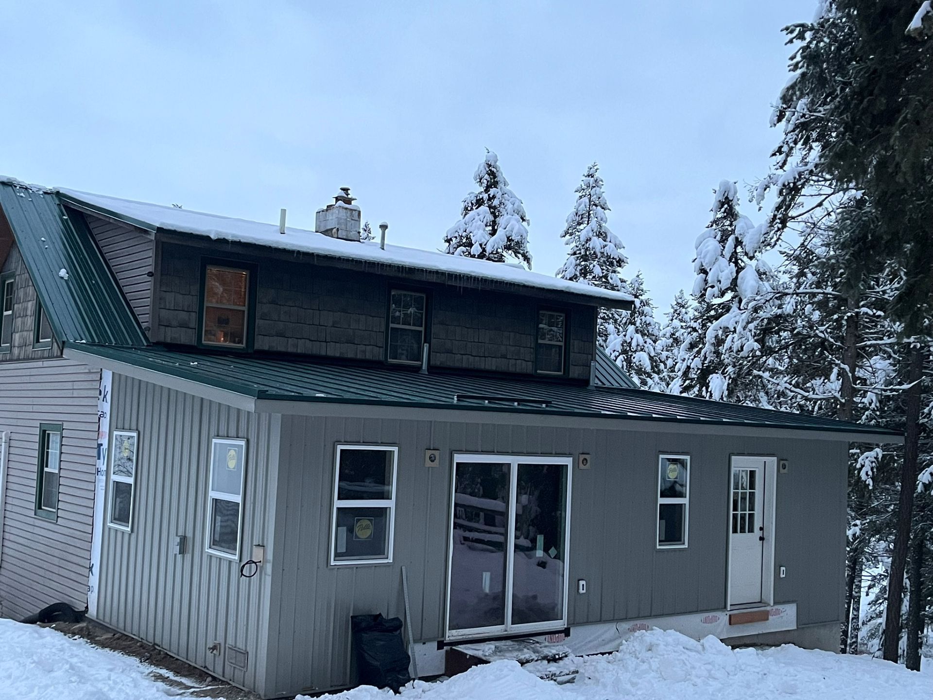 Snow-covered gray house with a dark roof and sliding glass door in a winter setting