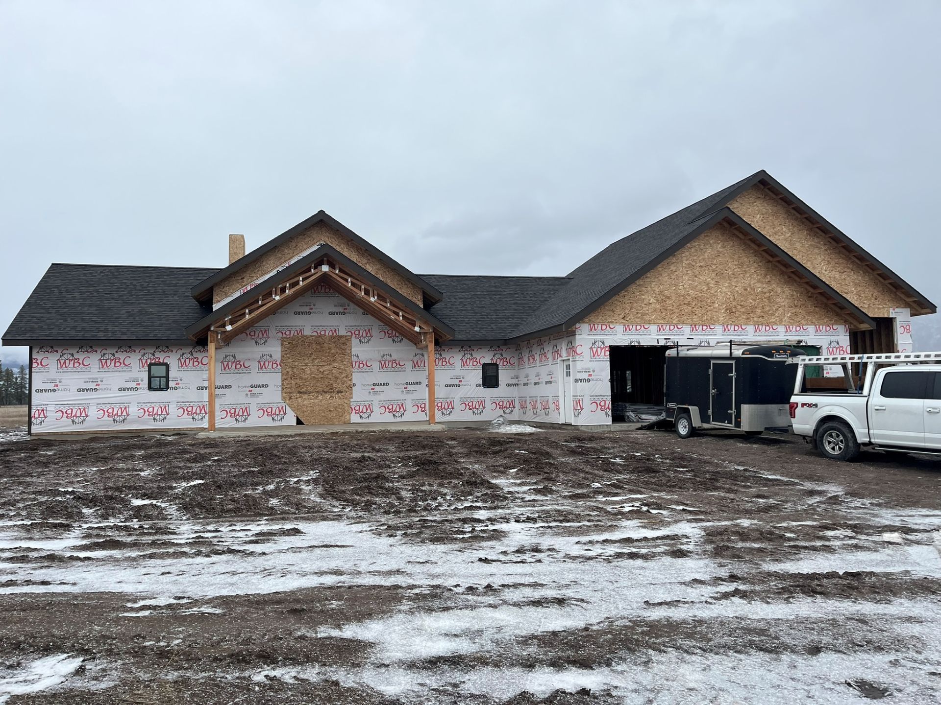 New house under construction with roof and siding installed, unfinished front yard, and a white pickup truck nearby