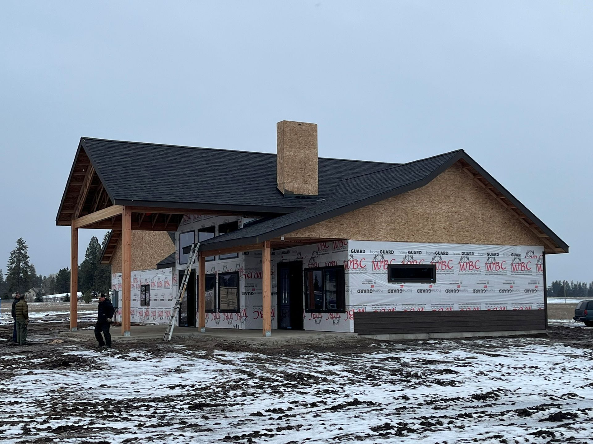 Half-built brick house with dark roof and chimney on a snowy construction site