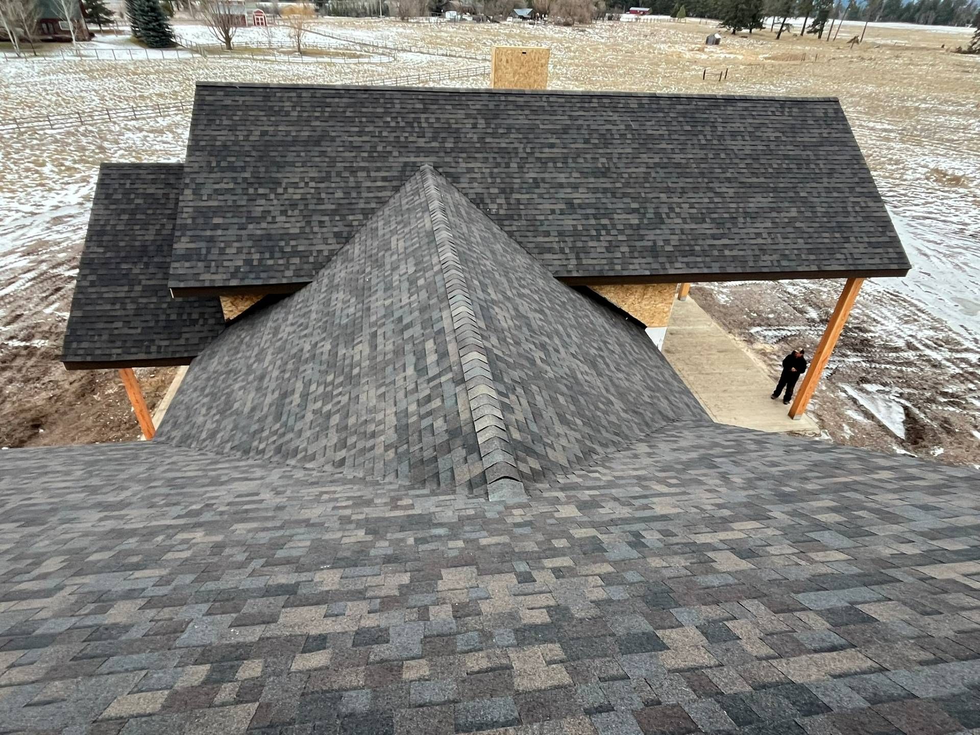 Rooftop view of dark gray shingle roofs with a snowy yard and a person standing at the right edge