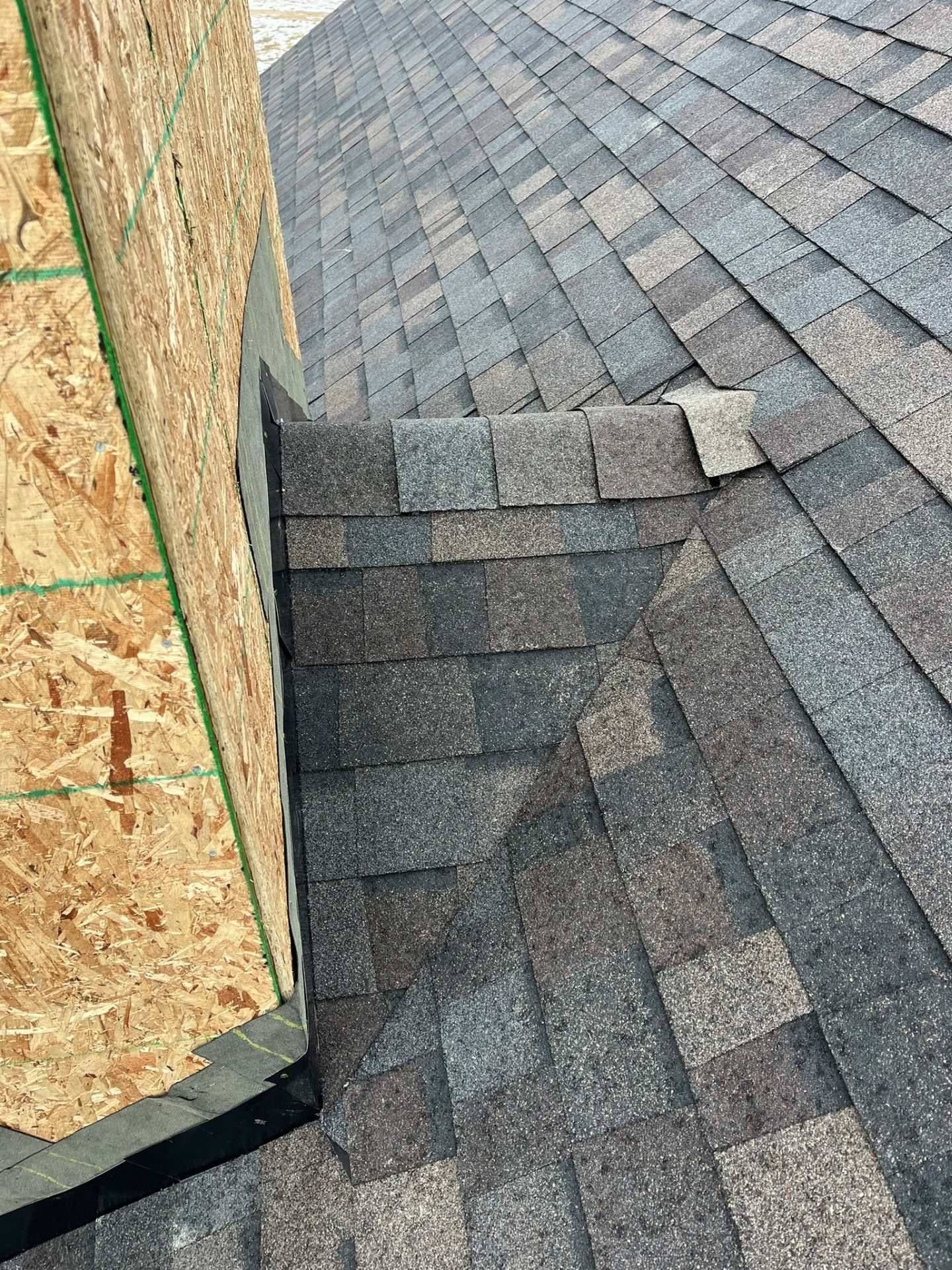 Roof shingles meeting a vertical wall with exposed plywood sheathing at the corner