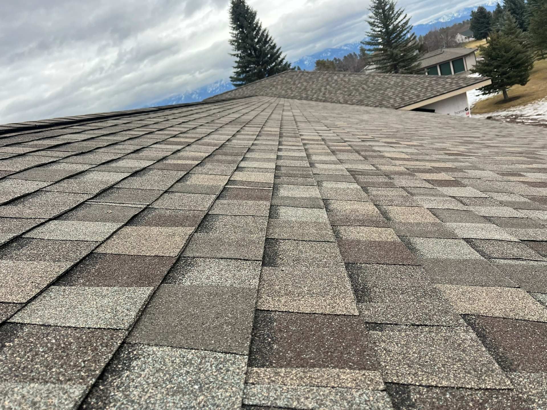 Shingled rooftop overlooking trees and mountains under a cloudy sky
