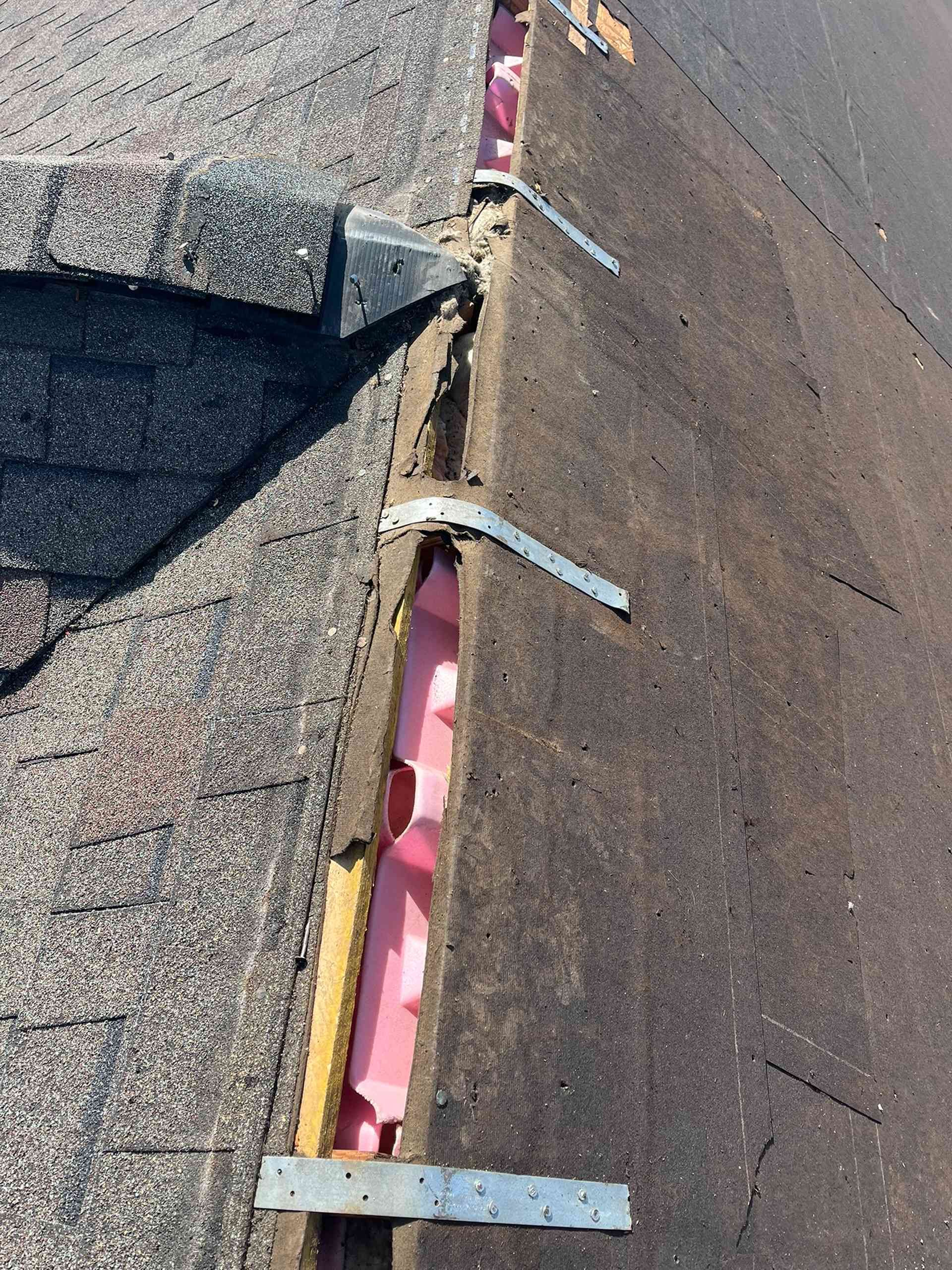Damaged roof seam with exposed pink underlayment and metal flashing strips between shingles