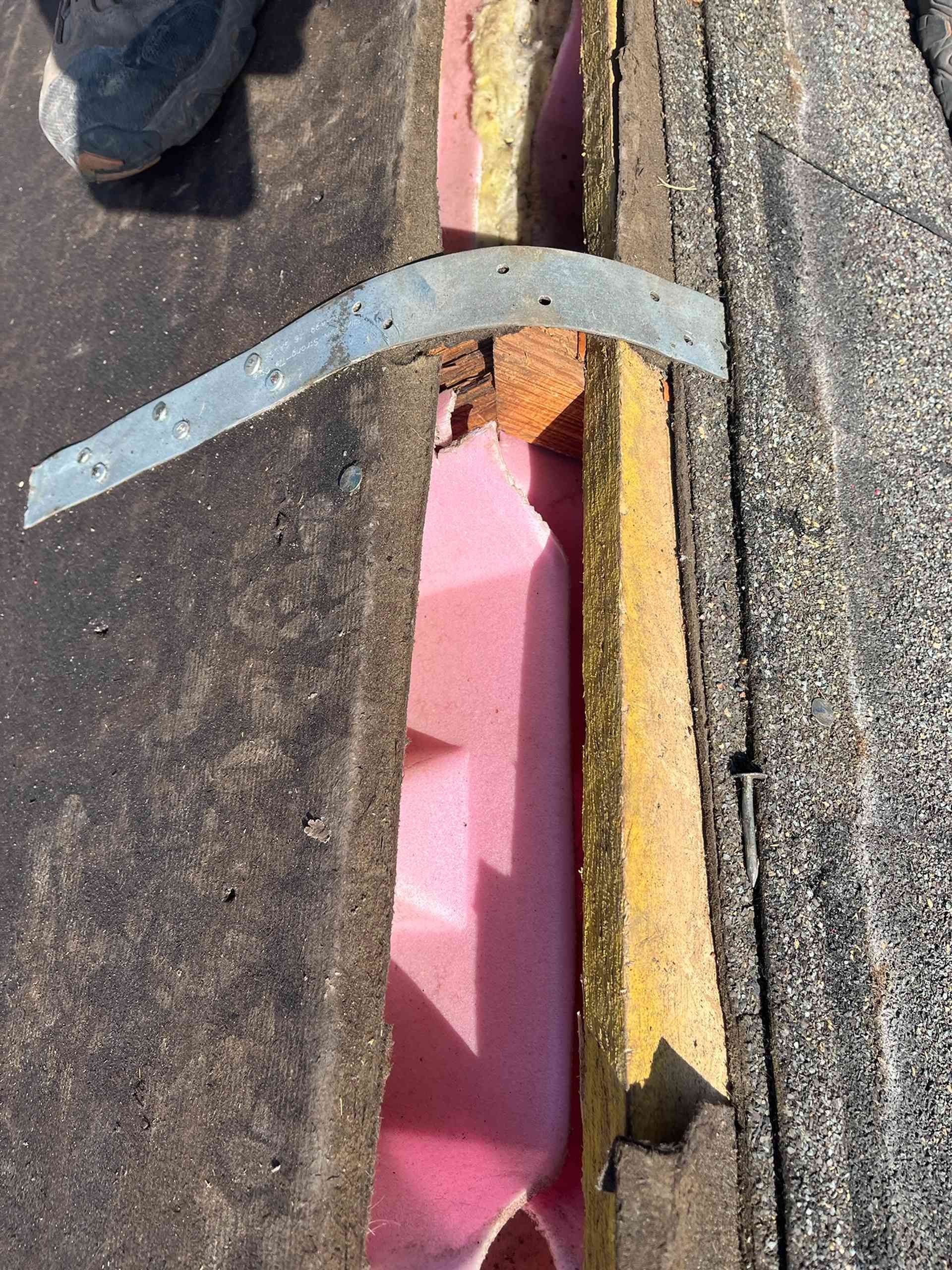 Damaged roof seam with exposed pink insulation and a curved metal flashing strip.