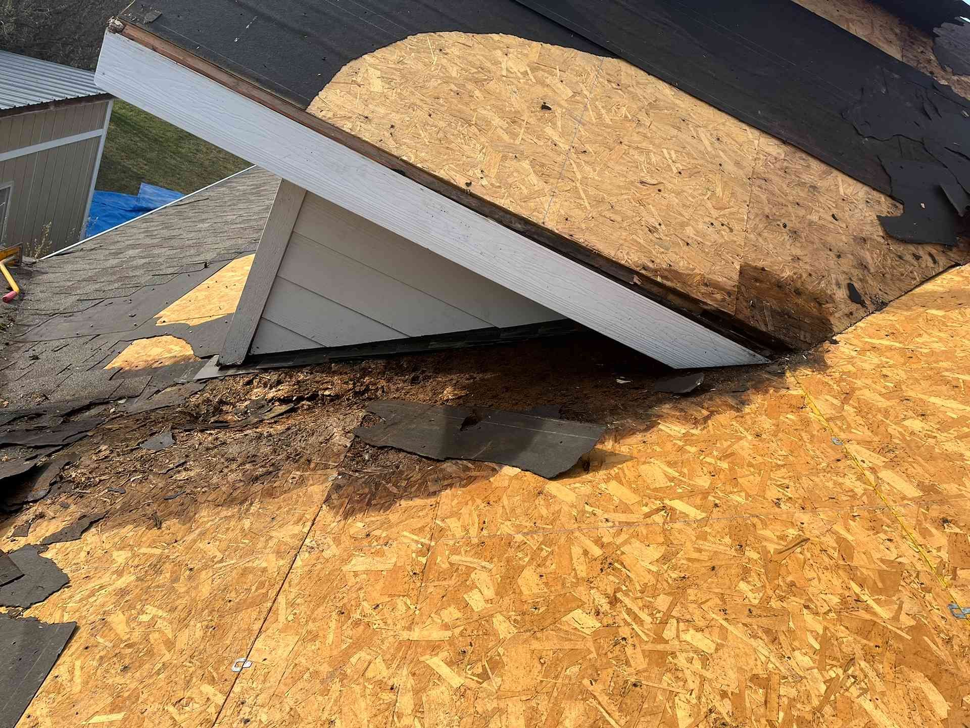 Storm-damaged roof with exposed plywood and a collapsed section over a white dormer