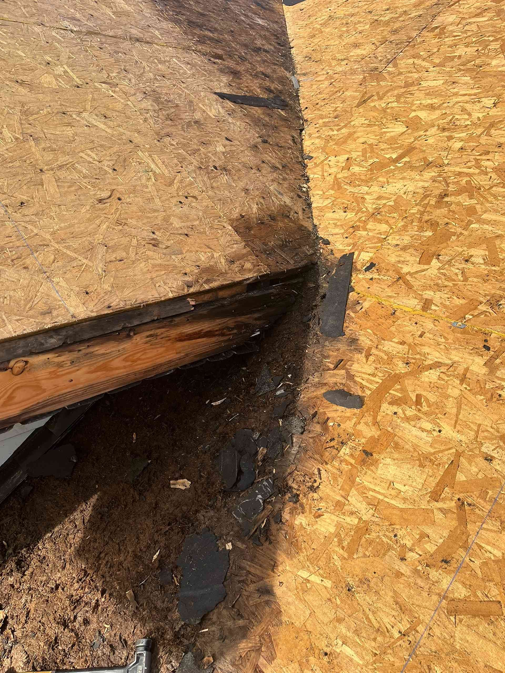 Close-up of a damaged roof seam with dark water stains between tan shingles.