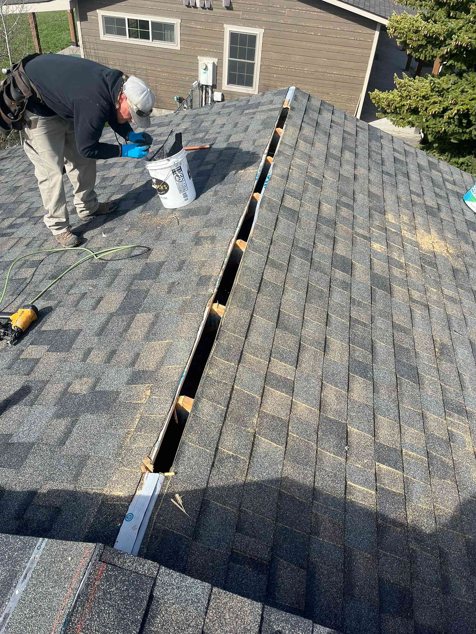 Worker repairing roof shingles on a house, with a long gap exposed between sections of roofing.