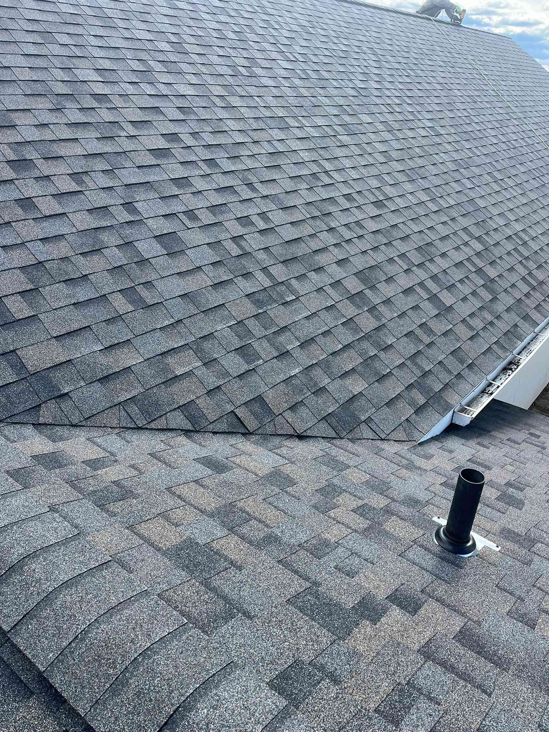 Roof shingles and a black vent pipe on a sloped gray roof