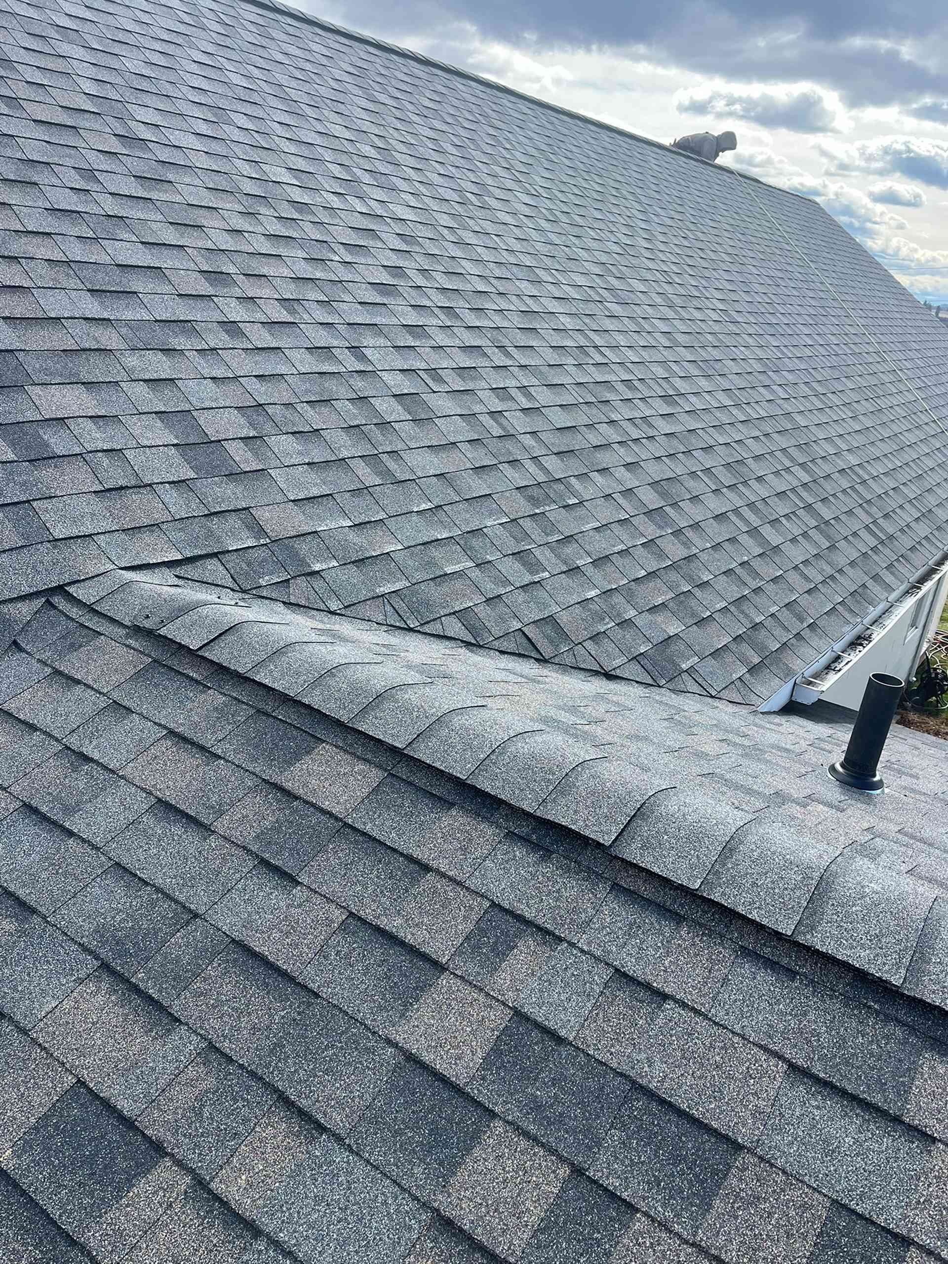 Gray shingled roof with a dormer and cloudy sky in the background