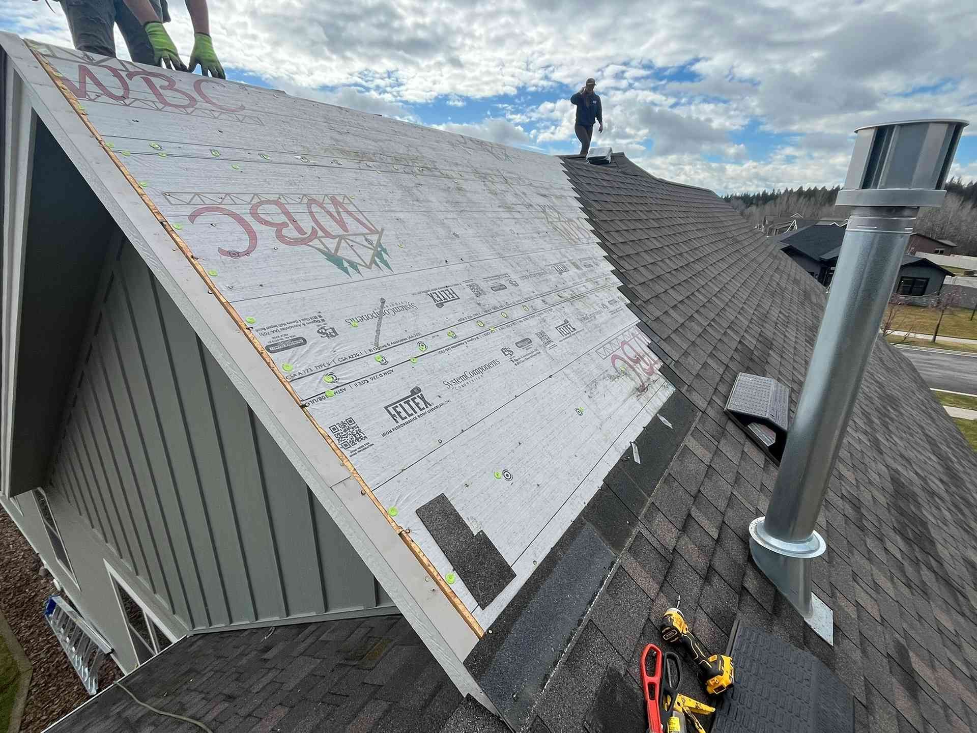 Roofing underlayment installed on a sloped roof, with tools and a roof vent under a partly cloudy sky