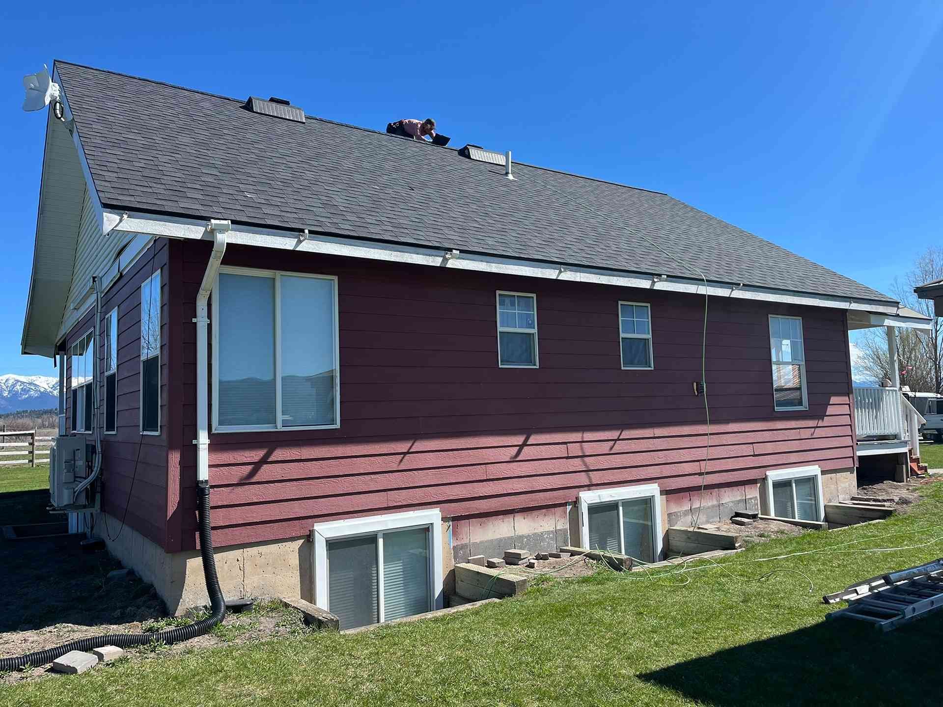Single-story maroon house with gray shingle roof and basement windows on a grassy lot.