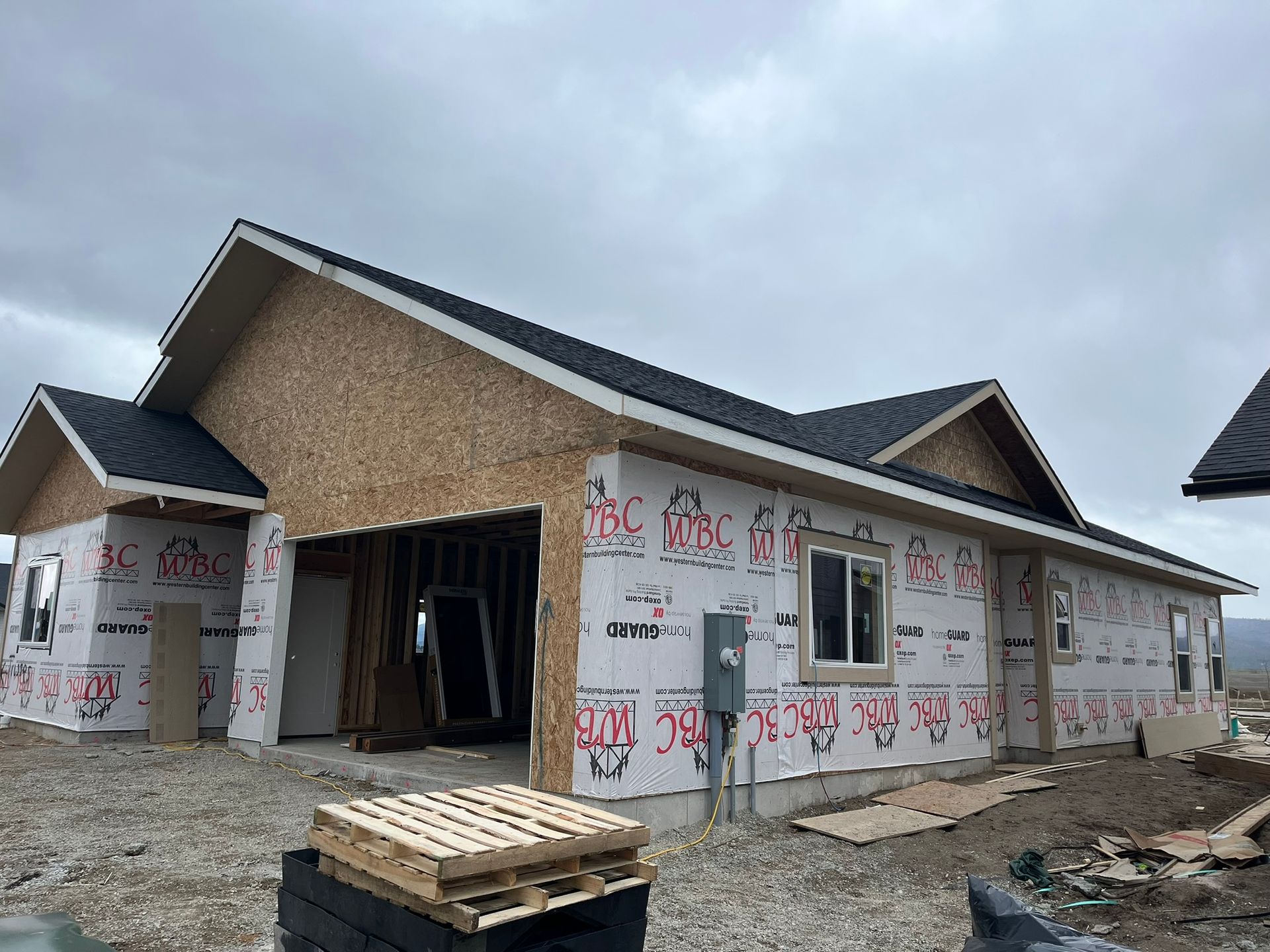 Partially built house with tan siding, dark roof, and exposed framing under construction outdoors