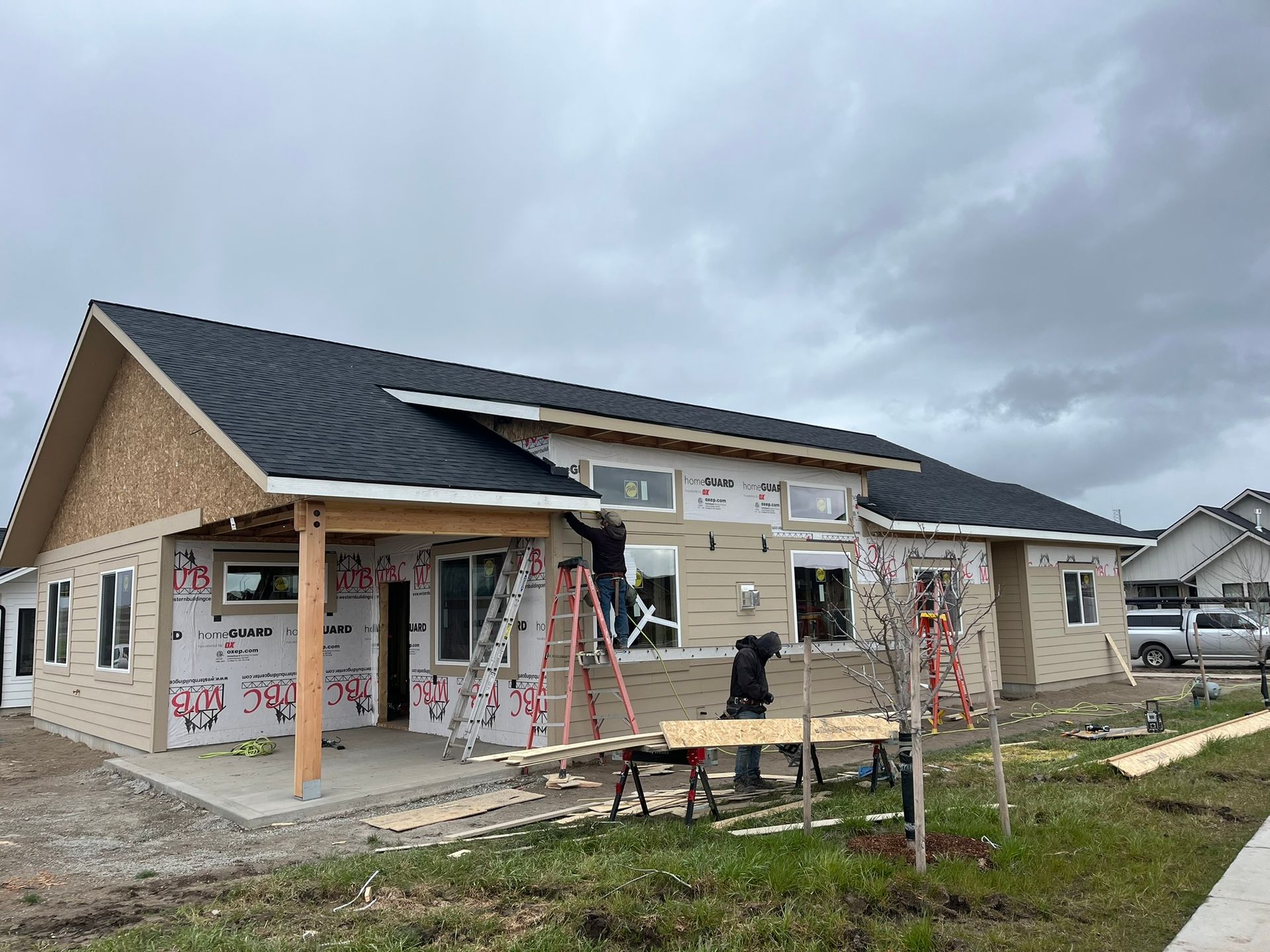 Single-story house under construction with exposed siding, scaffolding, and a cloudy sky.