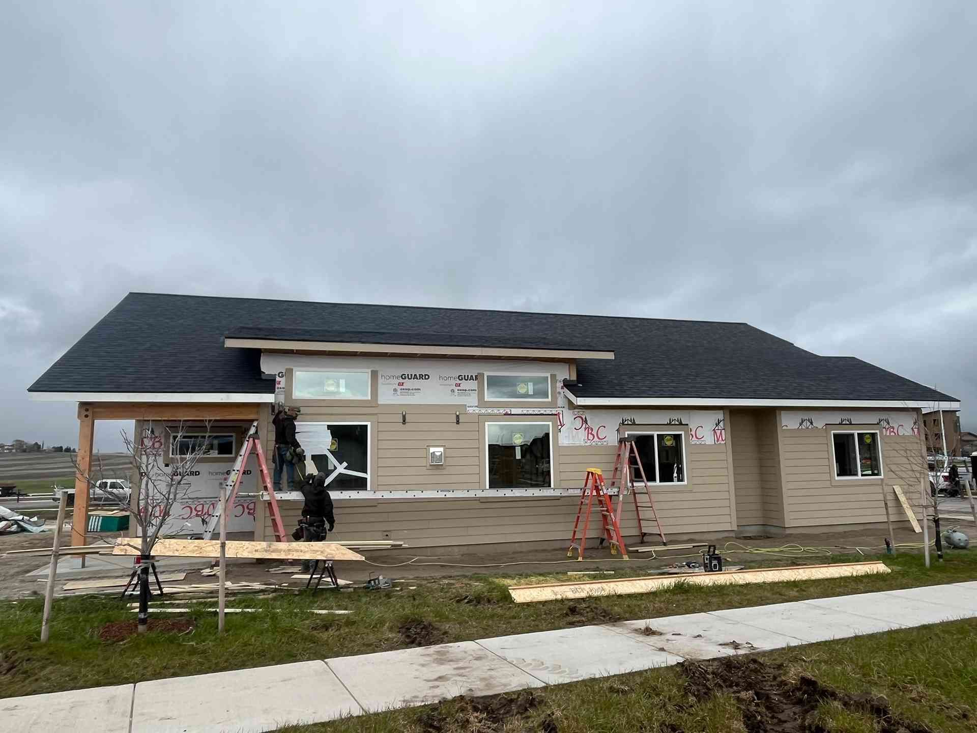 Single-story house under construction with workers, ladders, and scaffolding on a cloudy day