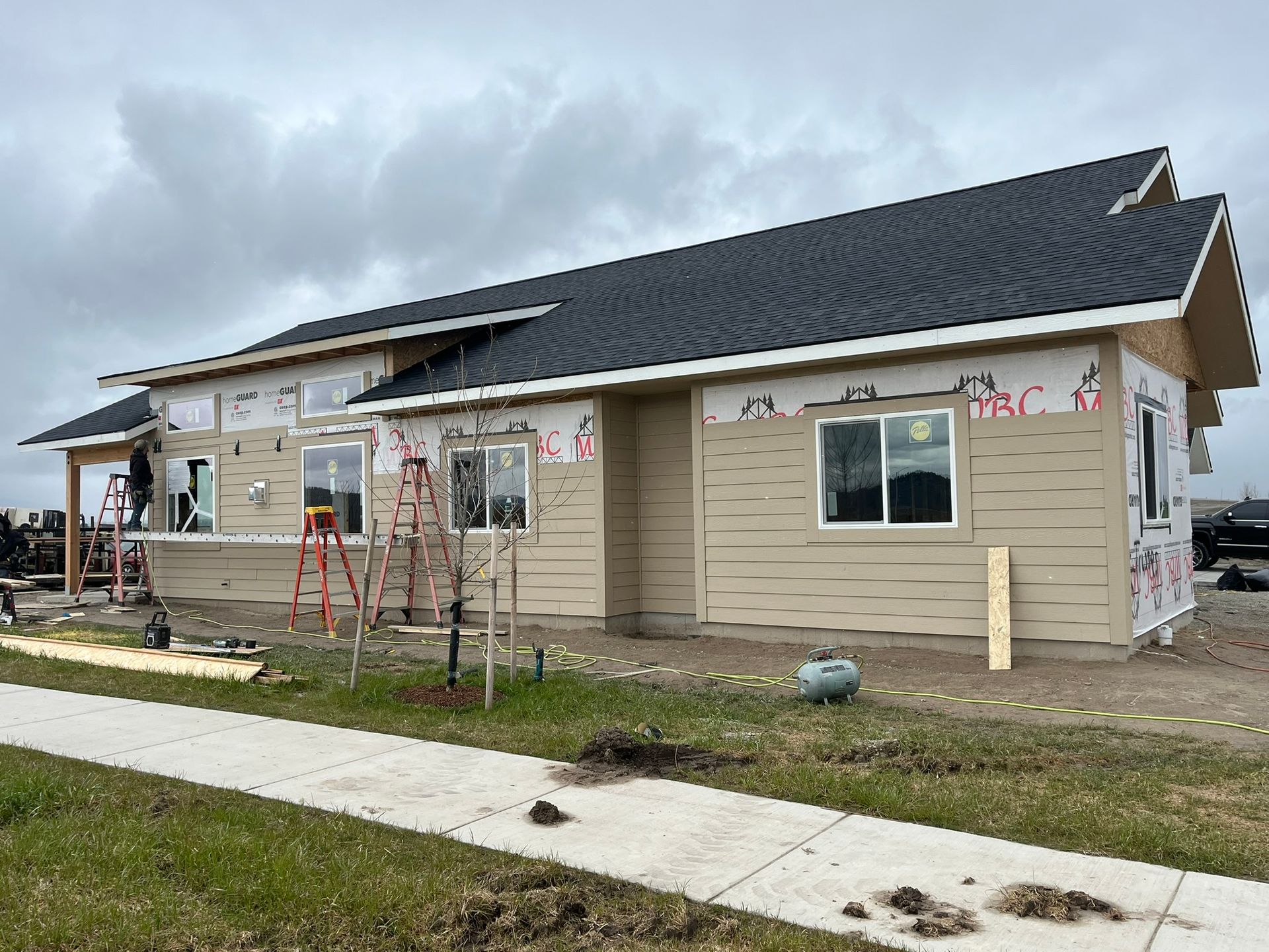 Single-story house under construction with beige siding, black roof, and ladders outside