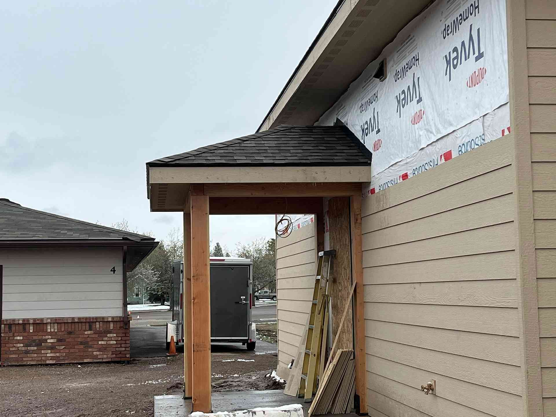Partially built house entry with wooden posts, siding, and construction materials outside.