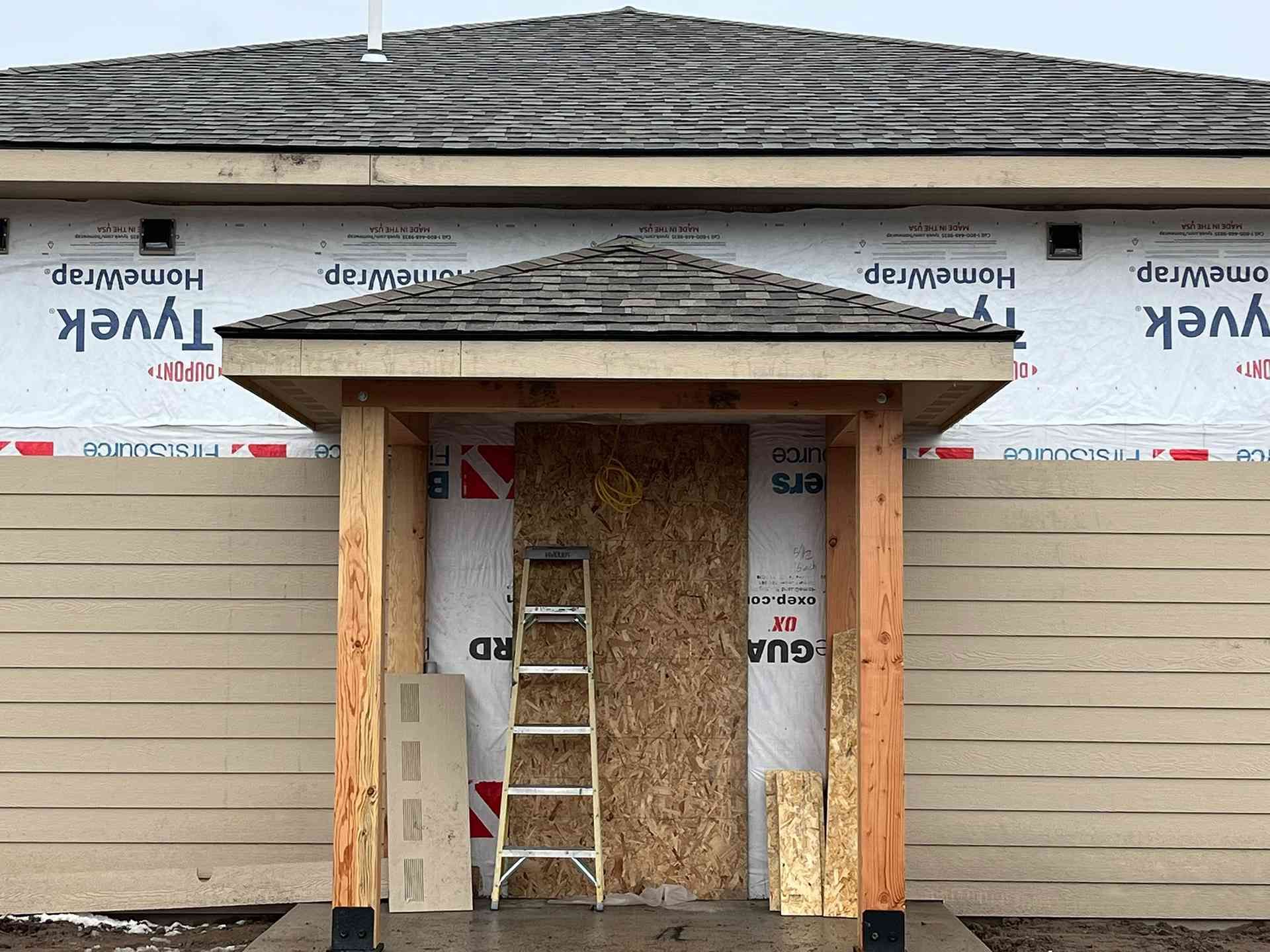 House exterior under construction with ladder in the front doorway and roofing materials exposed