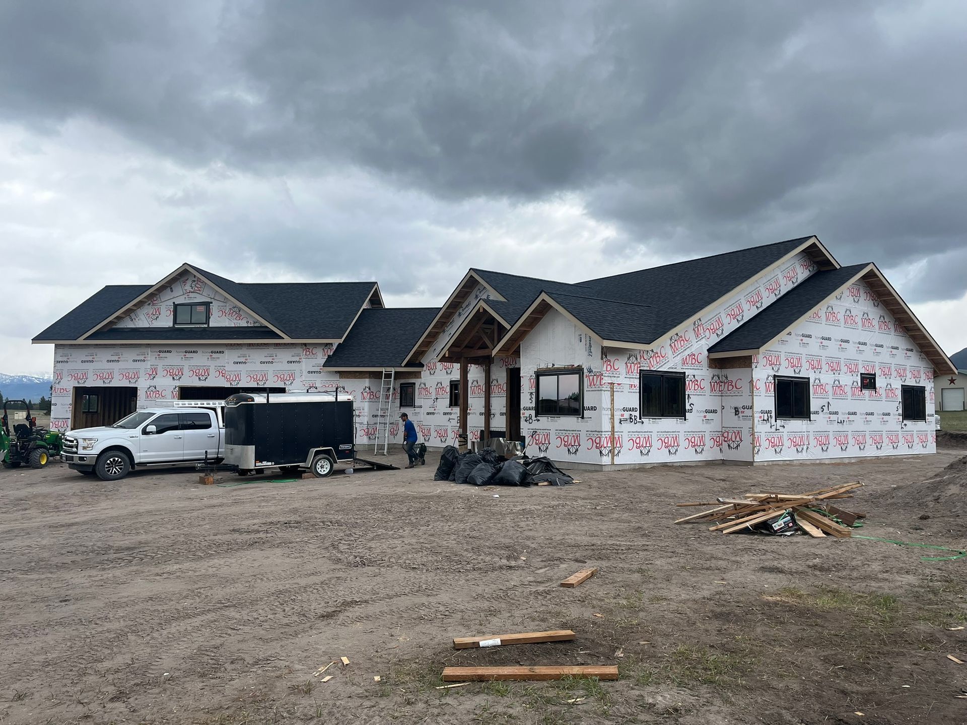 House under construction with white exterior wrap, parked truck, and cloudy sky.
