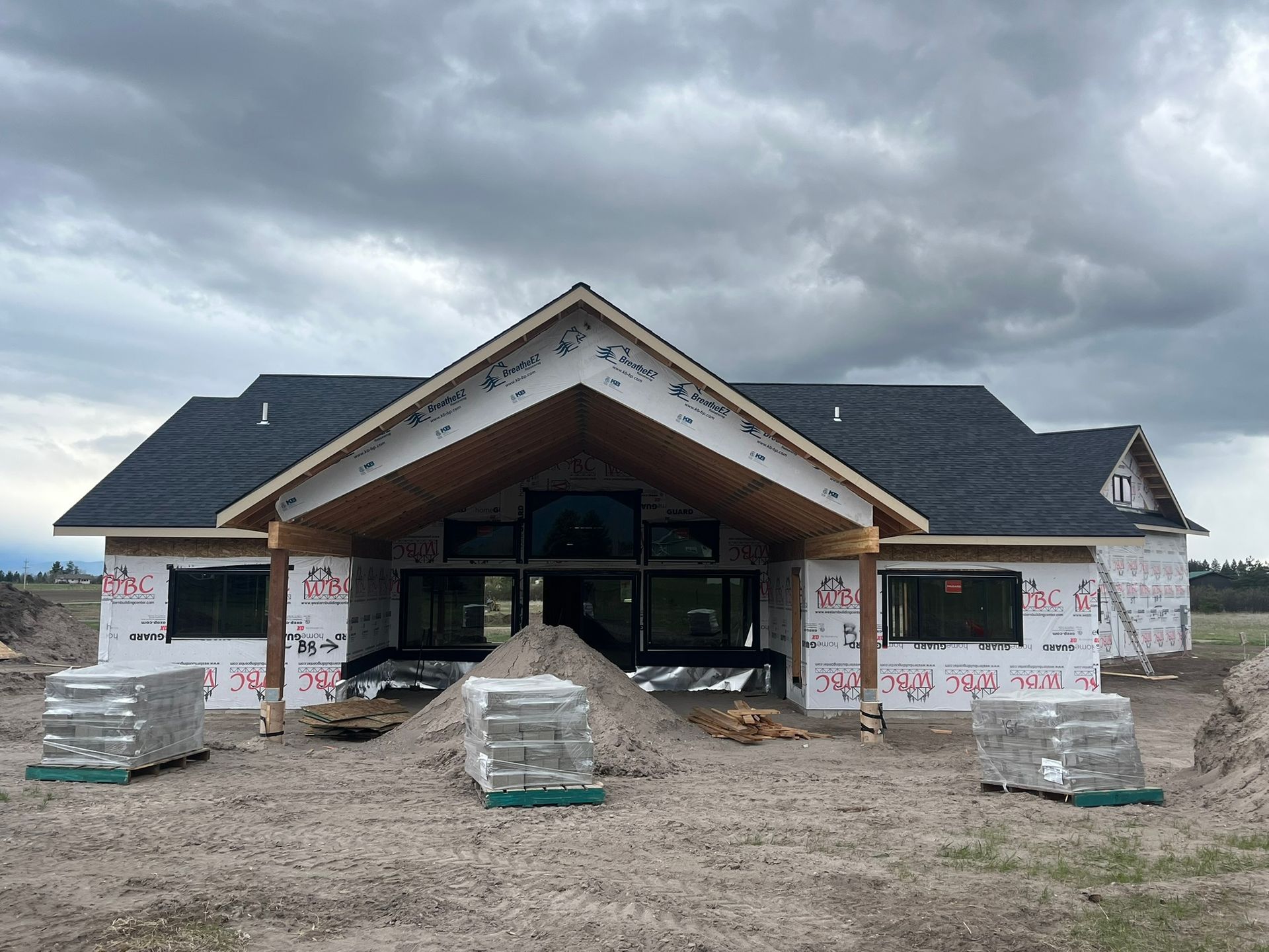 New house under construction with front porch, wrapped in house wrap and stacked materials in front