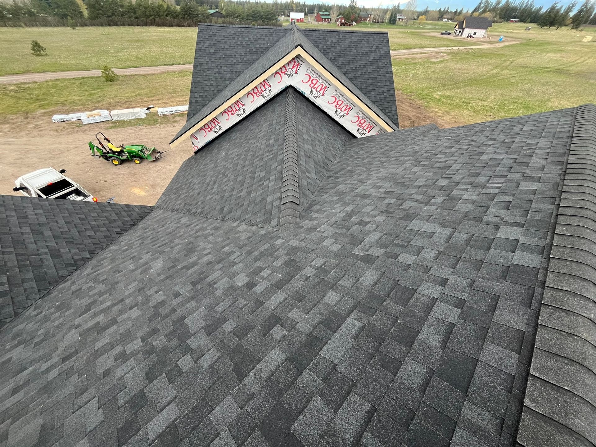 Roof with dark gray shingles and a small dormer, seen from above in a rural yard.