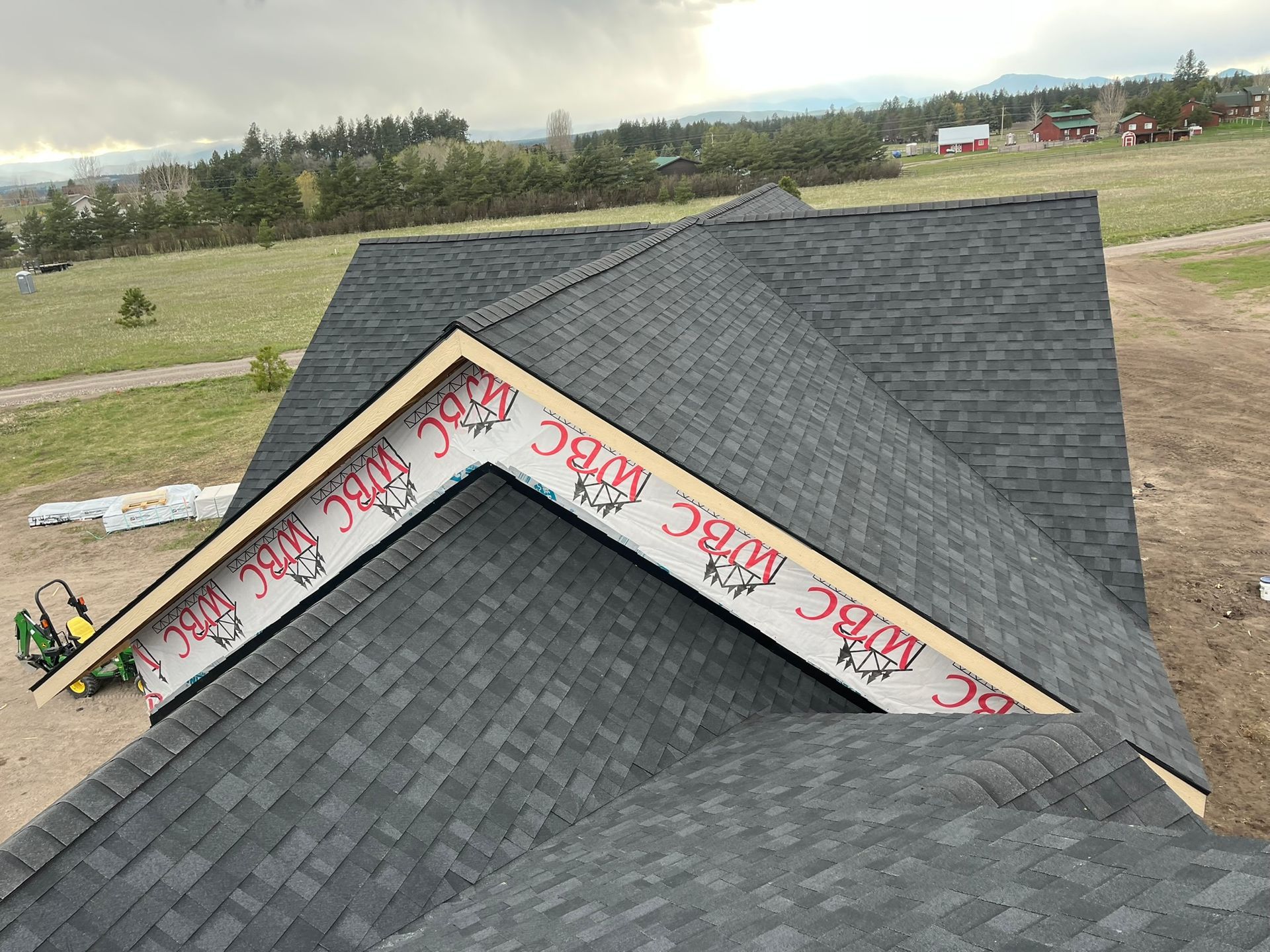 Roof under construction with gray shingles and wrapped valley flashing on a house in a grassy field