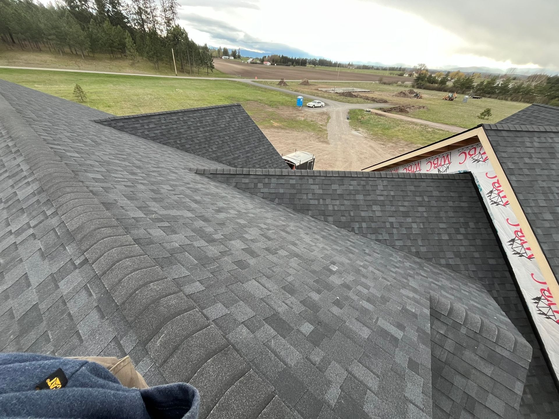 Roof shingles being installed on a house with a rural landscape in the background
