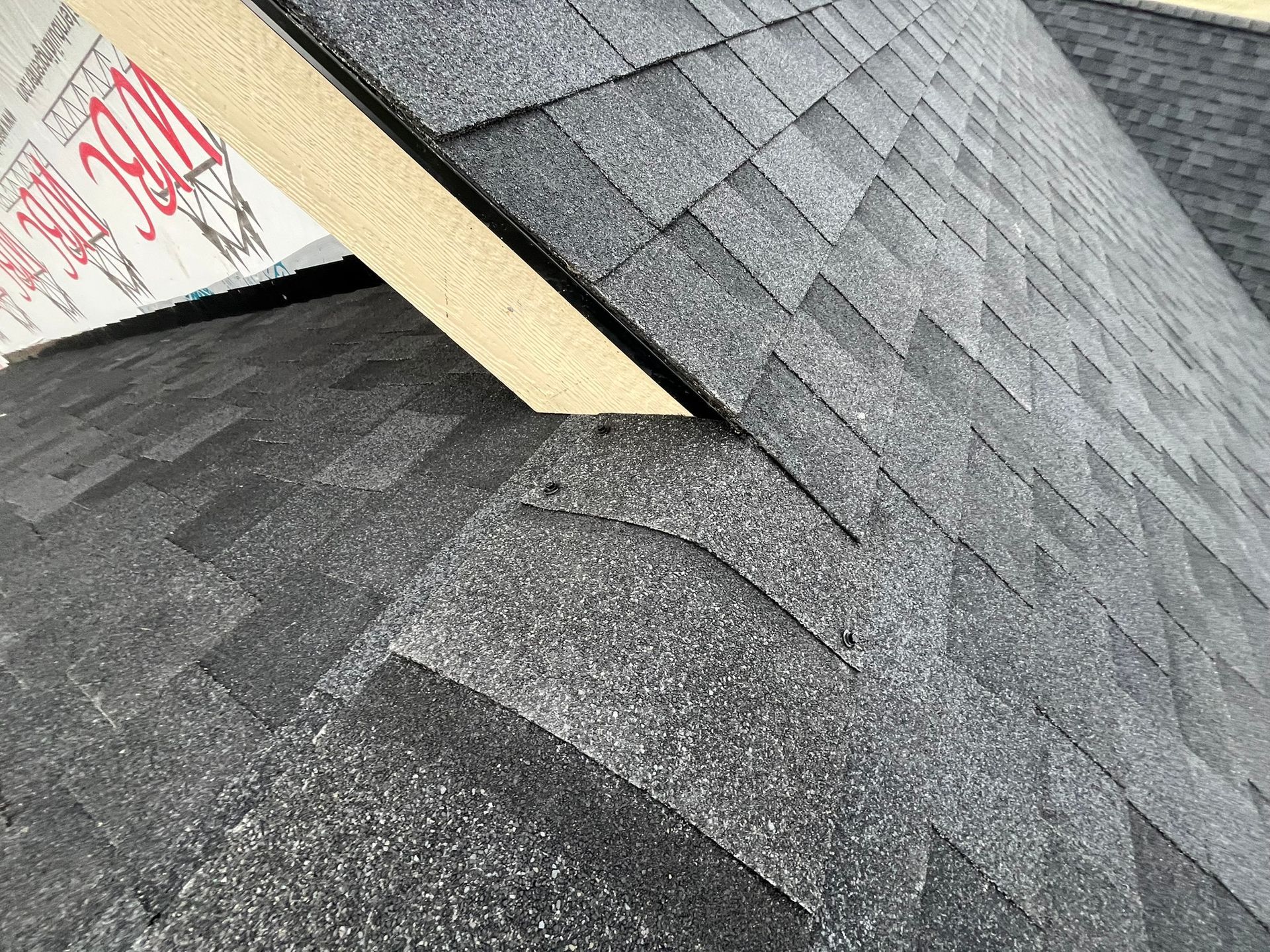 Roof shingles with a damaged gap exposing underlayment near a flashing seam.