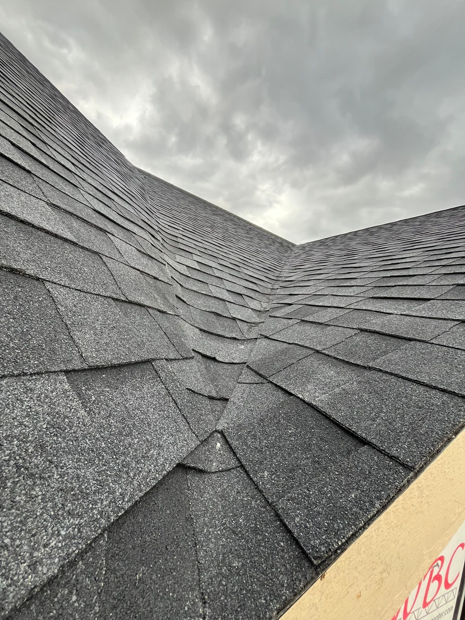 Close-up of a gray shingled roof with a steep peak under cloudy sky