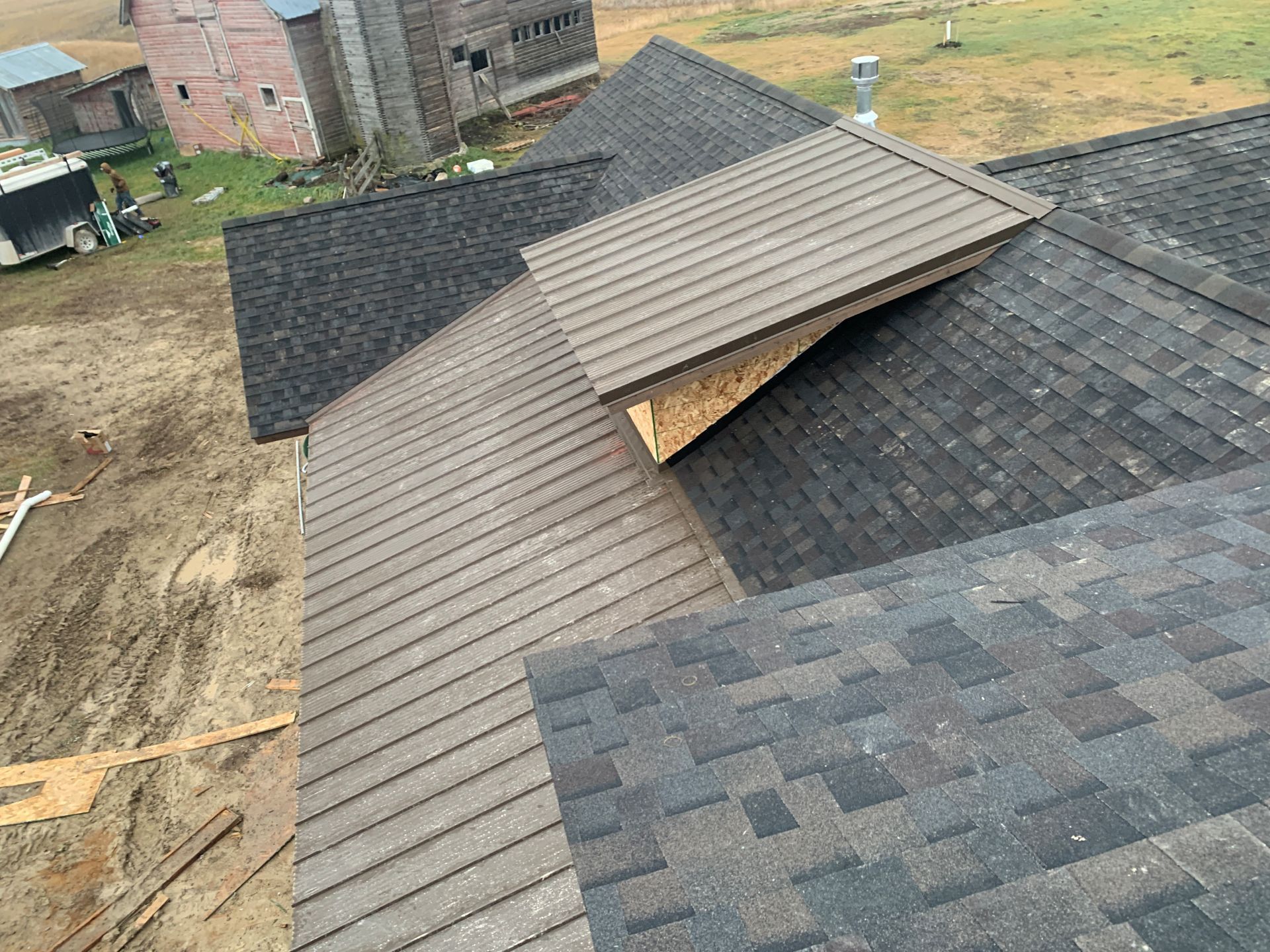 Roofing under construction with gray shingles and a tan section on a house in a yard