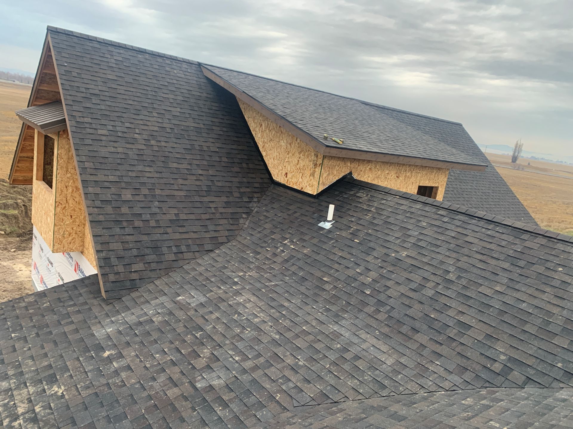 Aerial view of a house roof with dark shingles and a dormer on a cloudy day