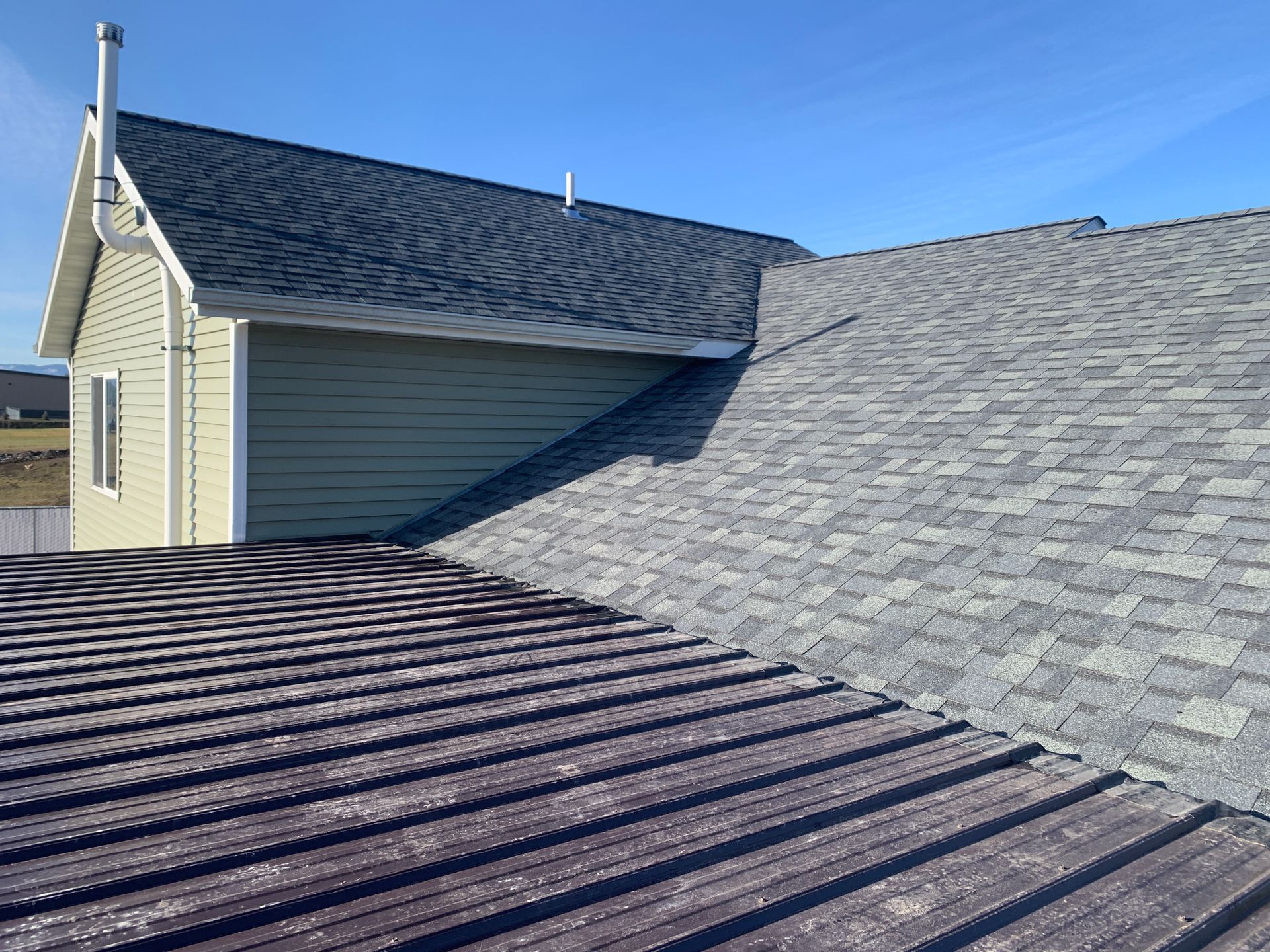 Close-up of two gray shingled residential roofs under a clear blue sky