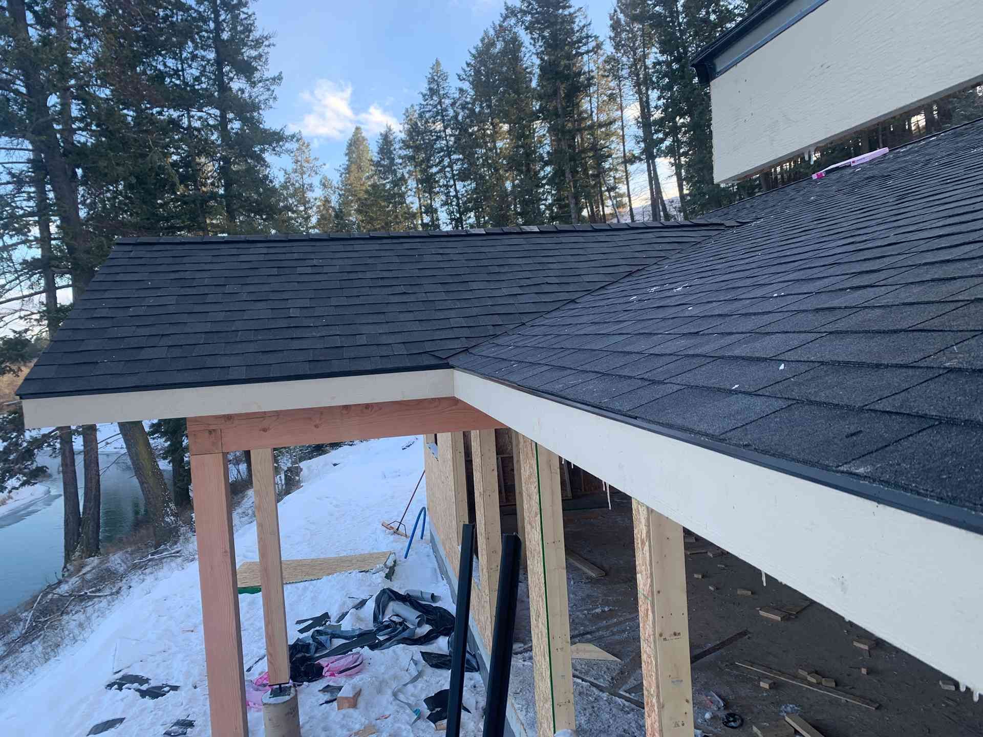 Partially finished porch roof with exposed framing and snow on the ground beside a house