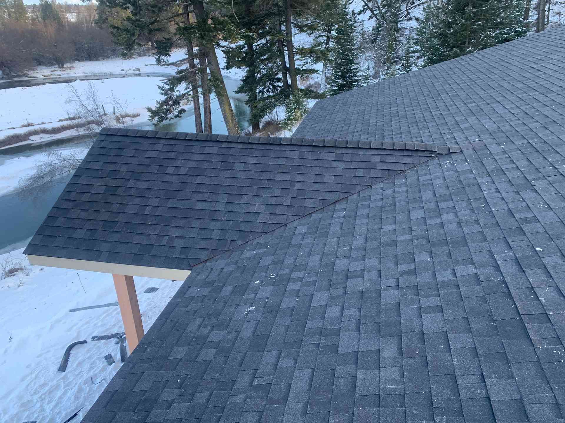 Fresh shingle roof with a lower attached section, viewed from above in a snowy wooded area