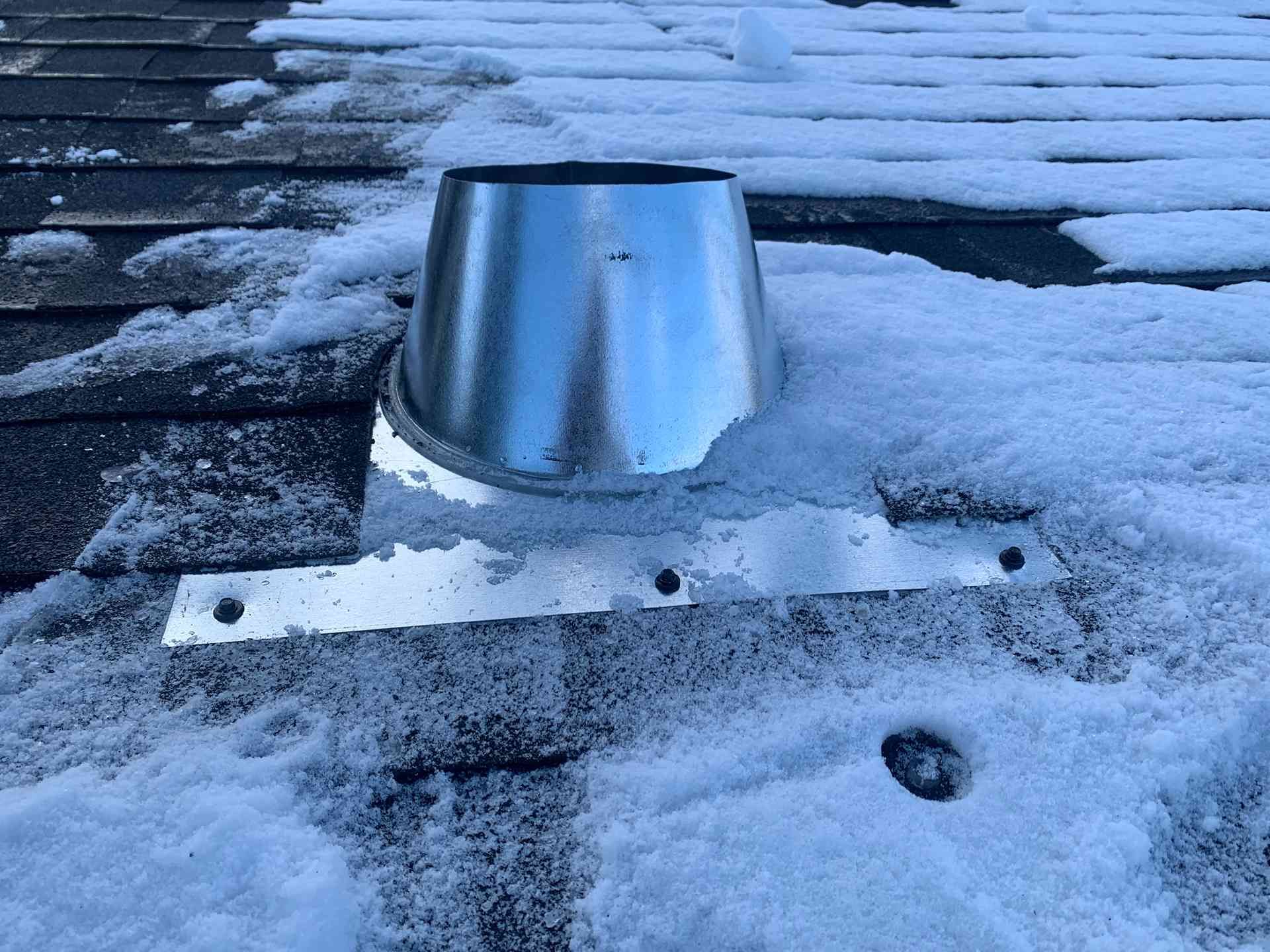 Metal rooftop vent on a snow-covered roof at dusk