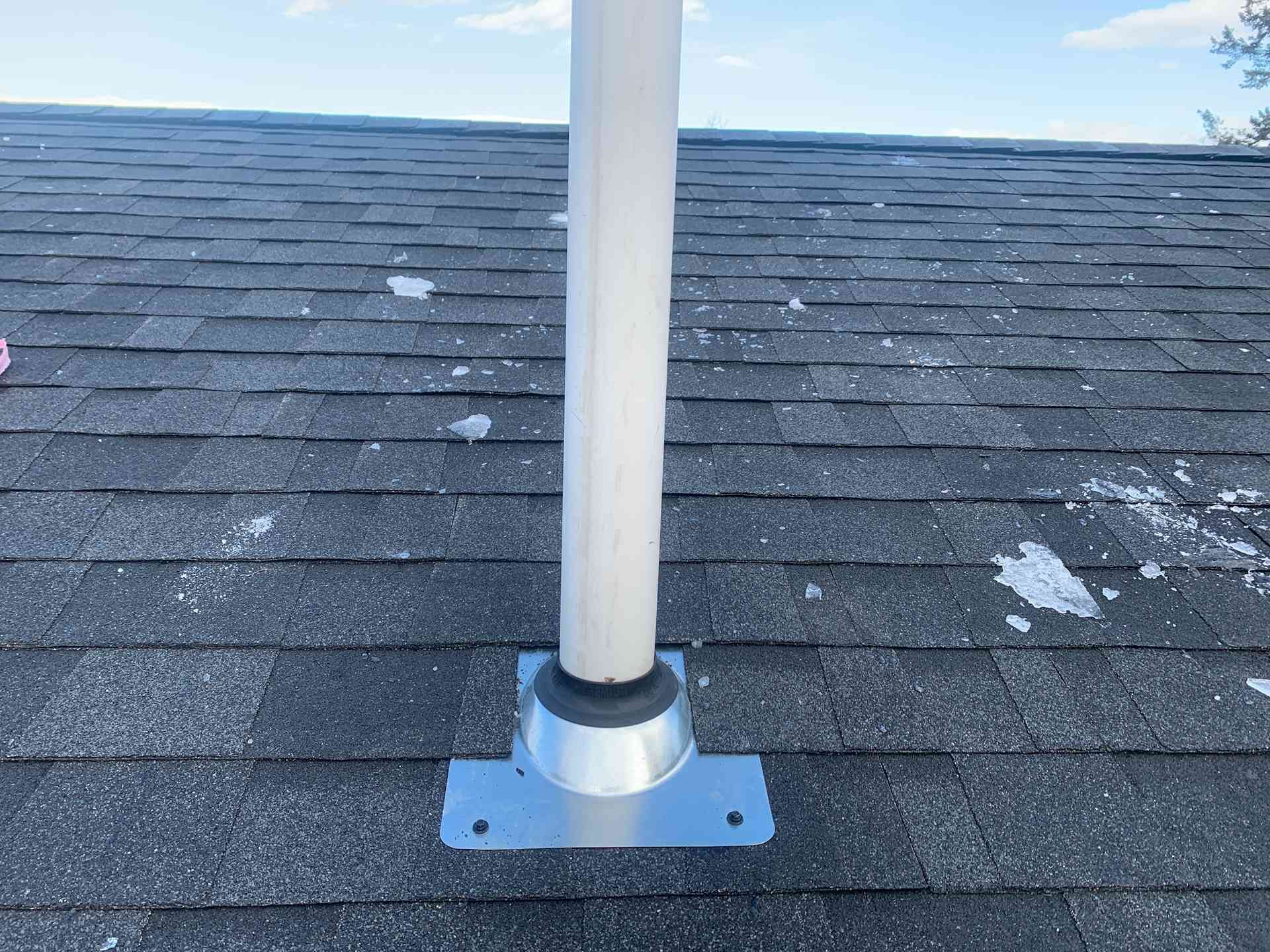 White flagpole mounted on a gray roof with dark shingles and patches of snow.