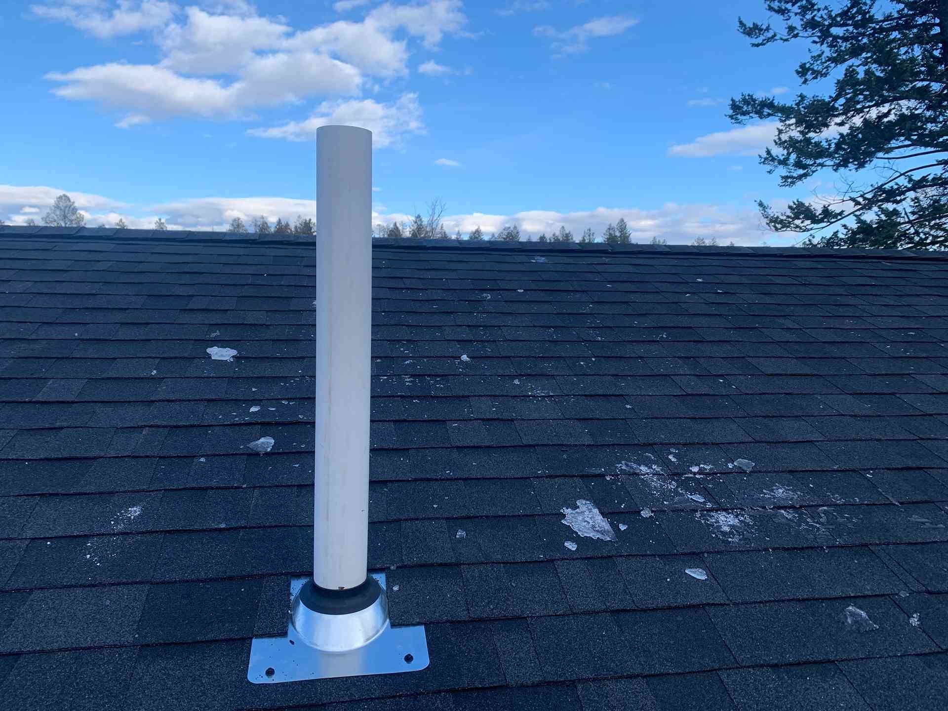 White vent pipe on a shingled roof under a blue sky