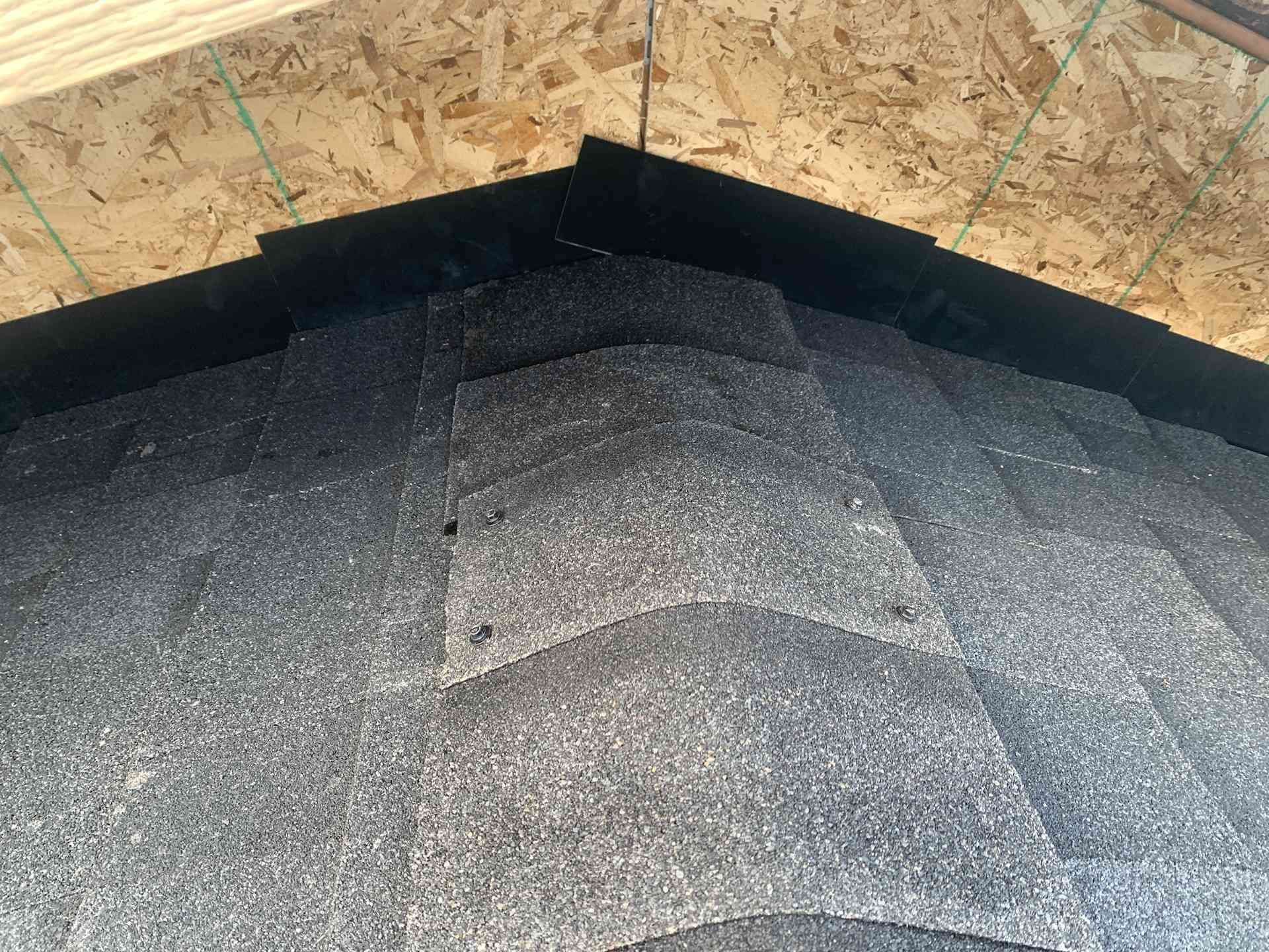 Close-up of a shingled roof edge beneath OSB plywood sheathing and black underlayment