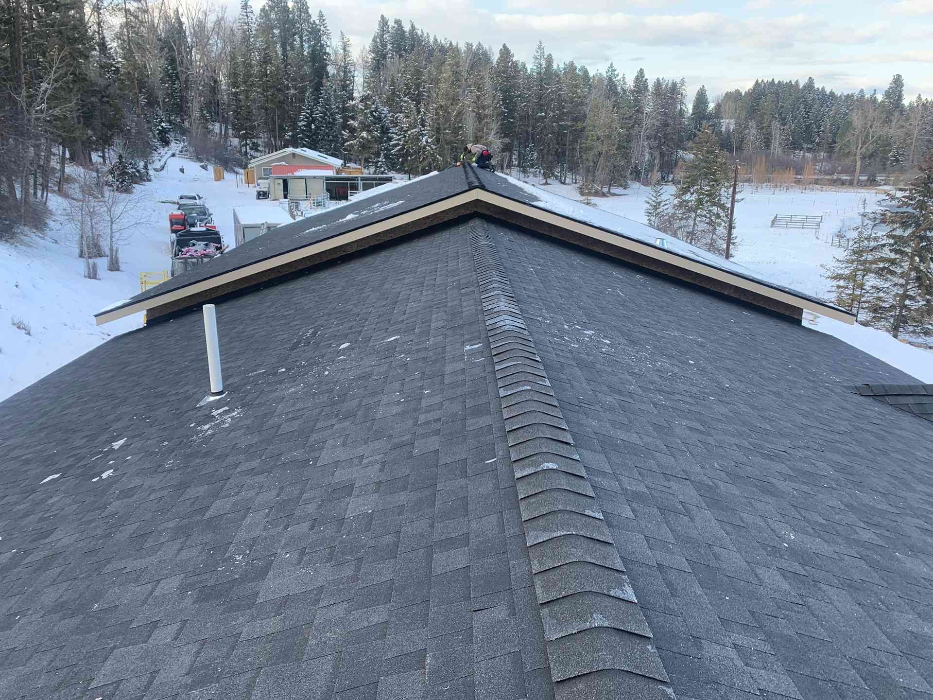 Snow-covered rooftop with a central ridge, overlooking a winter landscape with trees and houses