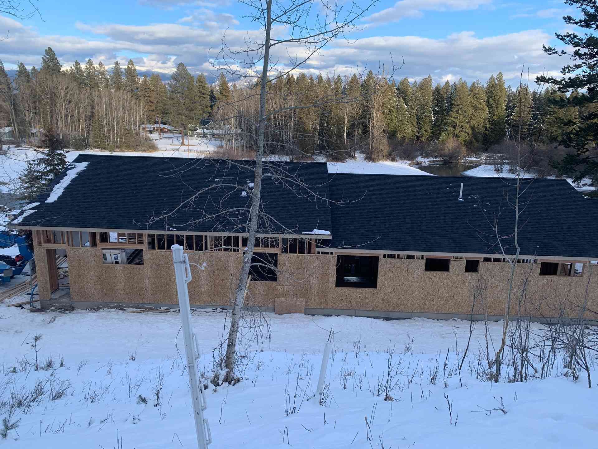 Snow-covered brick building with a dark roof and leafless trees in the foreground under a blue sky.
