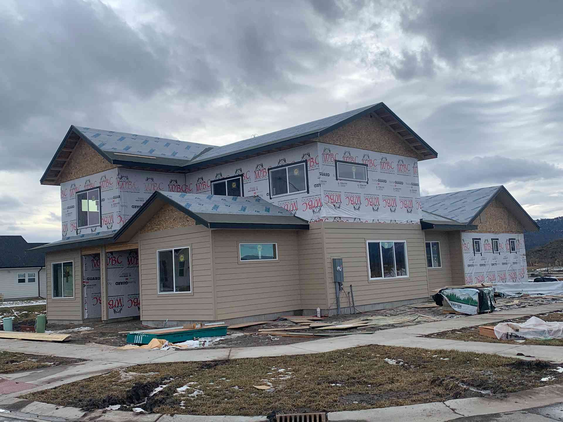 Partially built two-story house with unfinished siding and snow on the ground under a cloudy sky